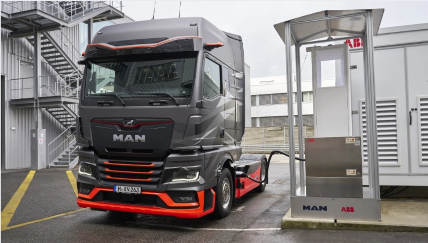 Elektrischer MAN-Lkw steht neben einer Ladestation von MAN und ABB in einem Industriegebiet mit nassem Boden.