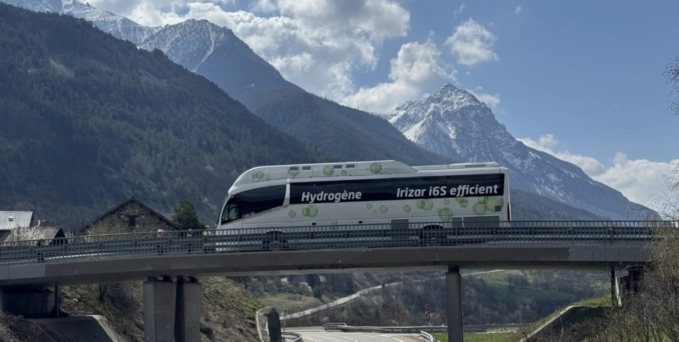 Weißer wasserstoffbetriebener Irizar i6S Efficient Bus fährt über eine Brücke, im Hintergrund schneebedeckte Berge.