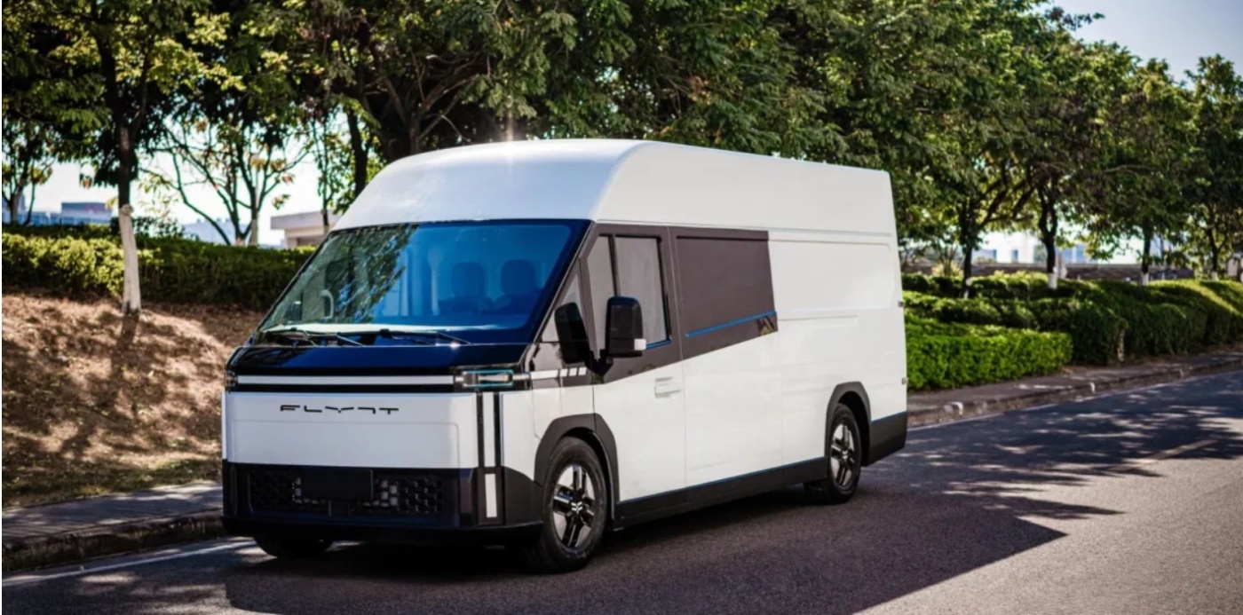 Moderner weißer Elektro-Lieferwagen mit der Aufschrift „FLYNT“ steht an einer von Bäumen und Sträuchern gesäumten Straße.