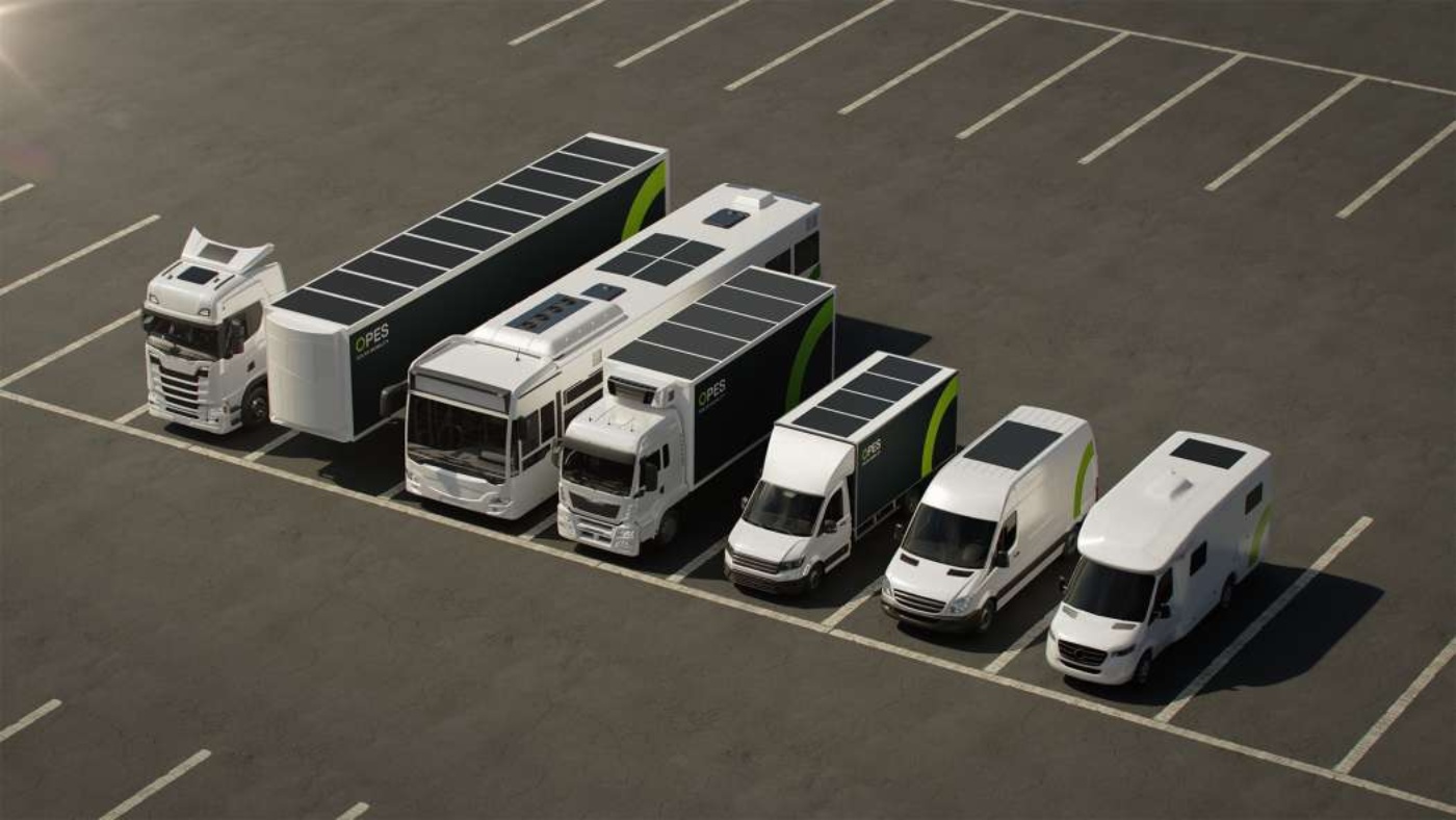 Sechs solarbetriebene Fahrzeuge vom Lkw bis zum Transporter stehen nebeneinander auf einem leeren Parkplatz, alle mit Solarpanels auf dem Dach.
