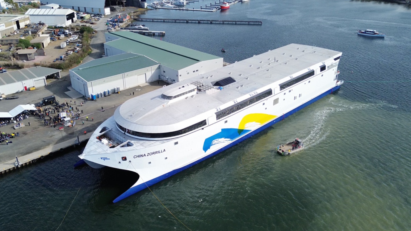 Große weiße Fähre namens „China Zorrilla“ liegt an einer Werft, mit einer Menschenmenge in der Nähe und kleineren Booten auf dem Wasser.