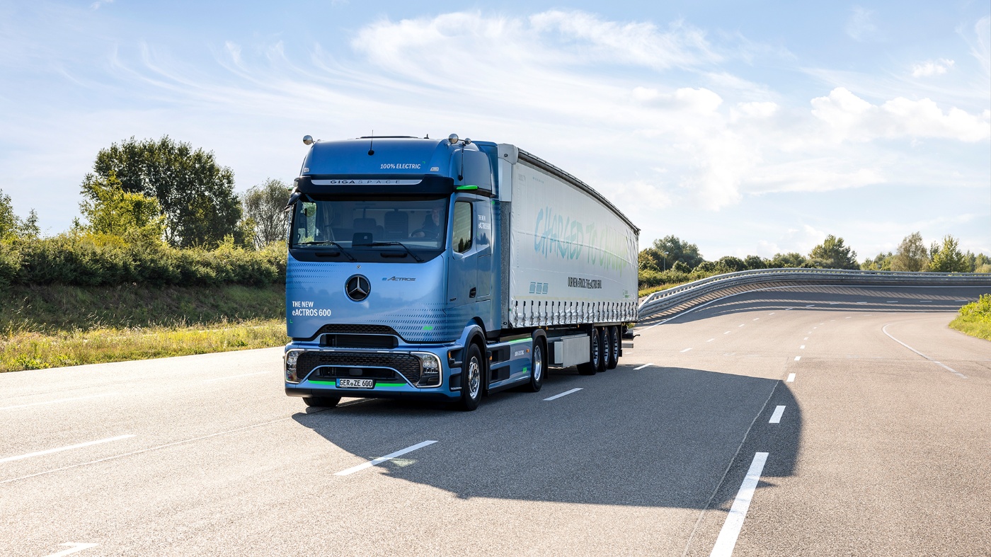 A blue electric Mercedes-Benz truck with trailer is driving on a test track under a sunny sky.