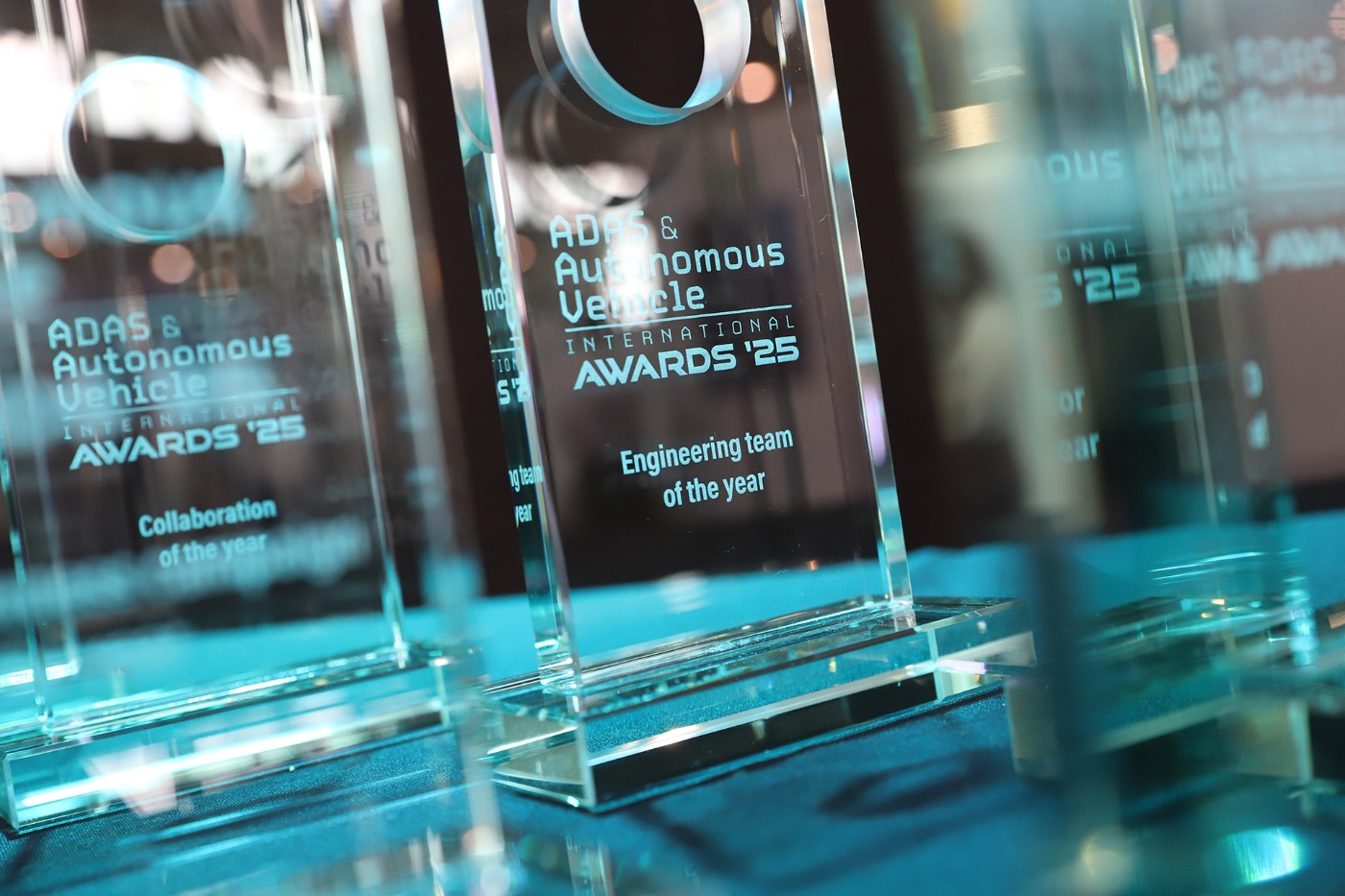 Several clear glass trophies labeled "ADAS & Autonomous Vehicle Awards 2025" on a table.