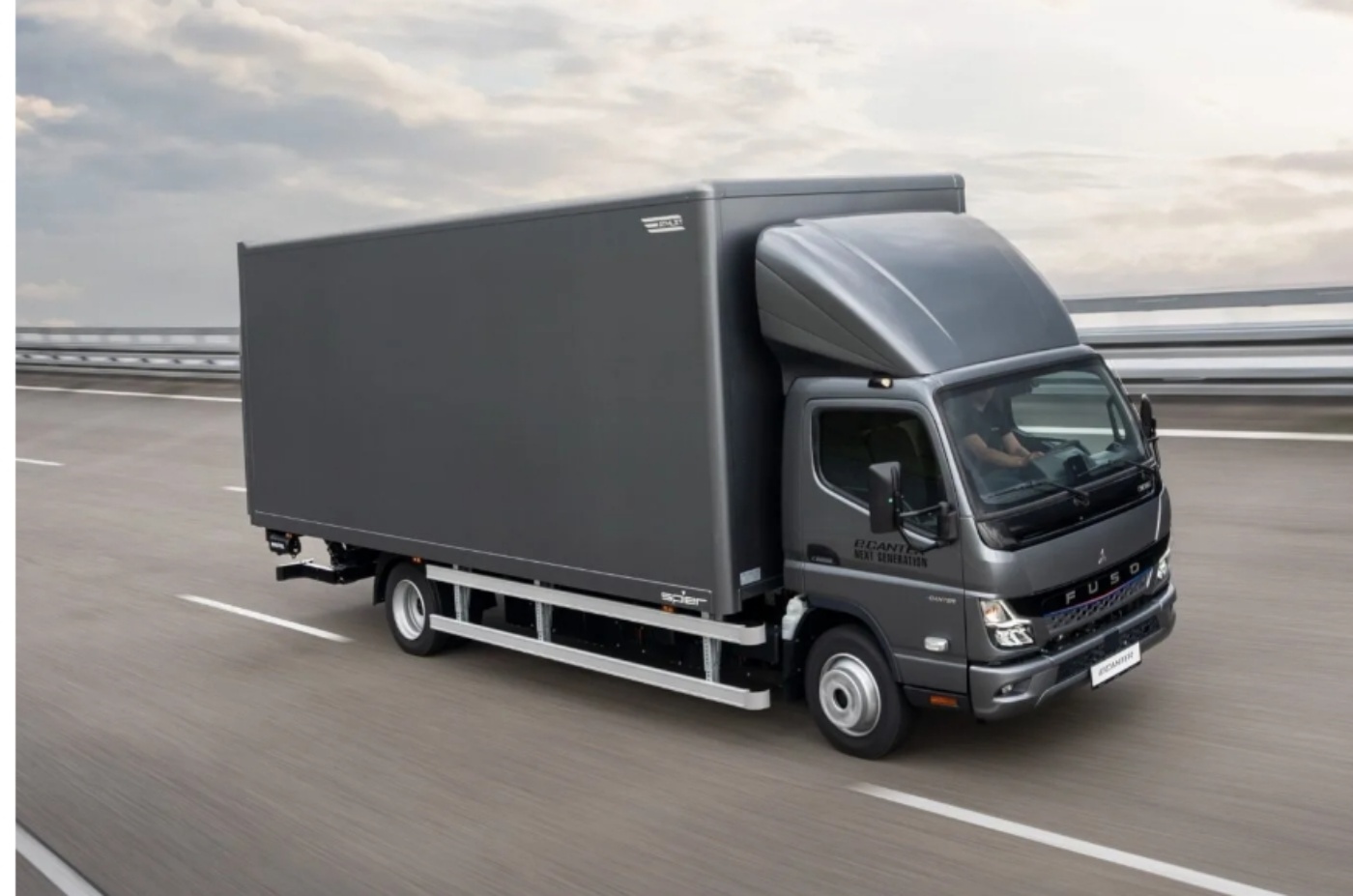 Dark grey delivery truck driving on a highway with a blurred background.