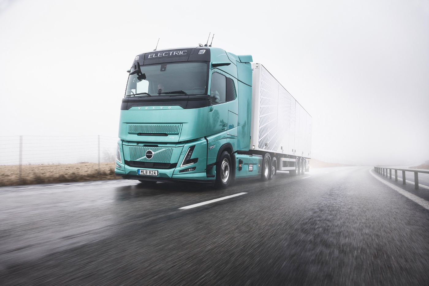 Electric Volvo truck driving on a wet road in foggy weather.