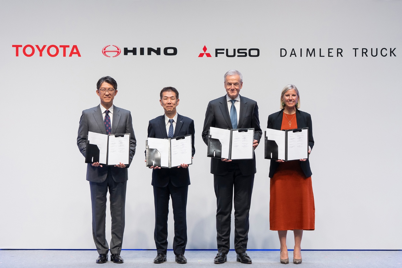 Vier Führungskräfte halten unterzeichnete Dokumente vor Logos von Toyota, Hino, Fuso und Daimler.