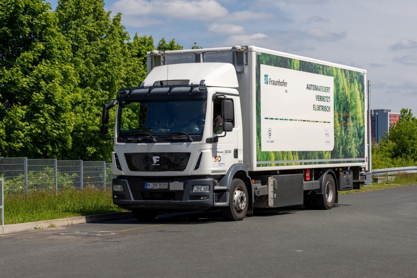 Elektro-Lieferwagen mit Fraunhofer-Logo steht auf einer Straße neben Grünflächen.
