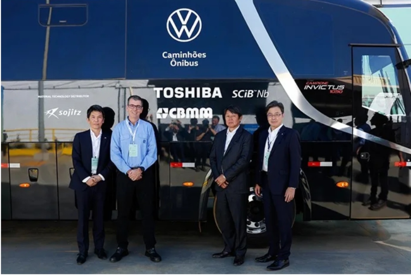 Vier Männer stehen vor einem Volkswagen-Bus mit Toshiba- und CBMM-Logos.
