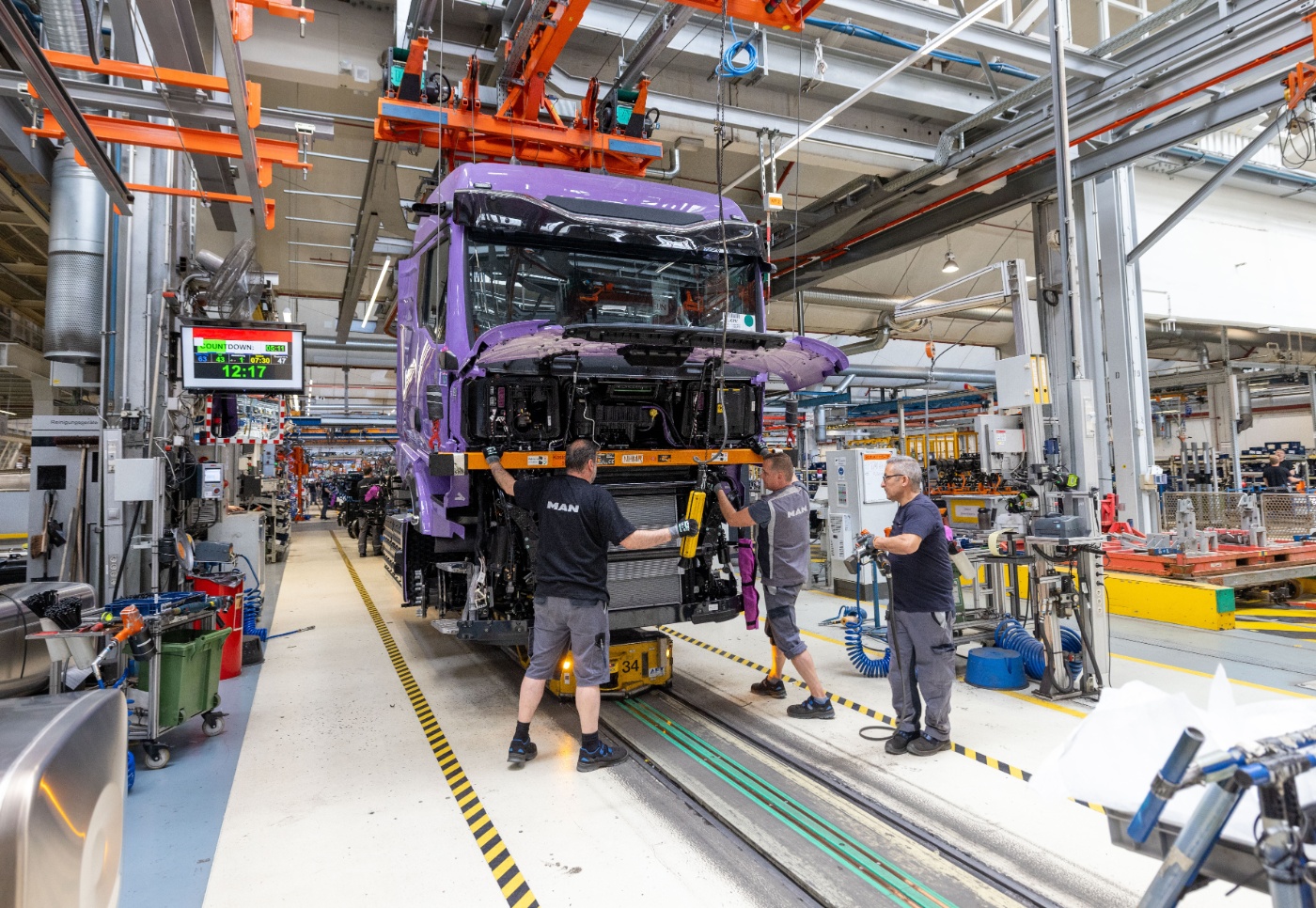 Mitarbeiter montieren eine violette Lkw-Kabine am Fließband in einer Fabrikhalle.