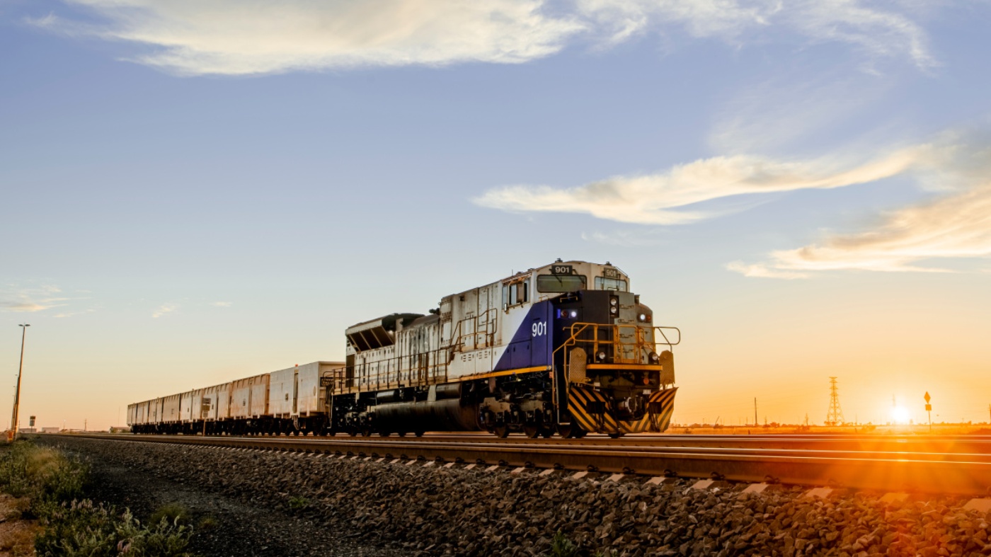 Freight train on railway track at sunset with clear sky and warm lighting.