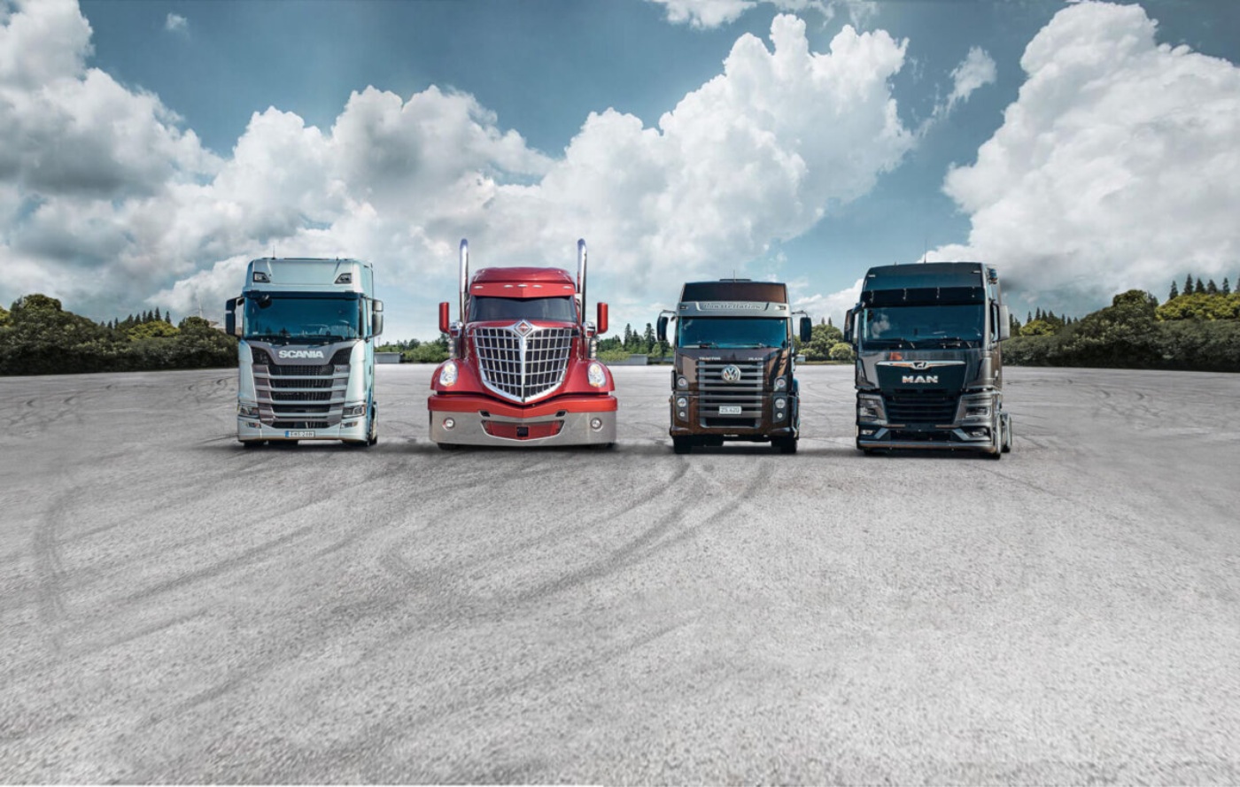 Four modern trucks from different brands are lined up side by side on an open asphalt area.