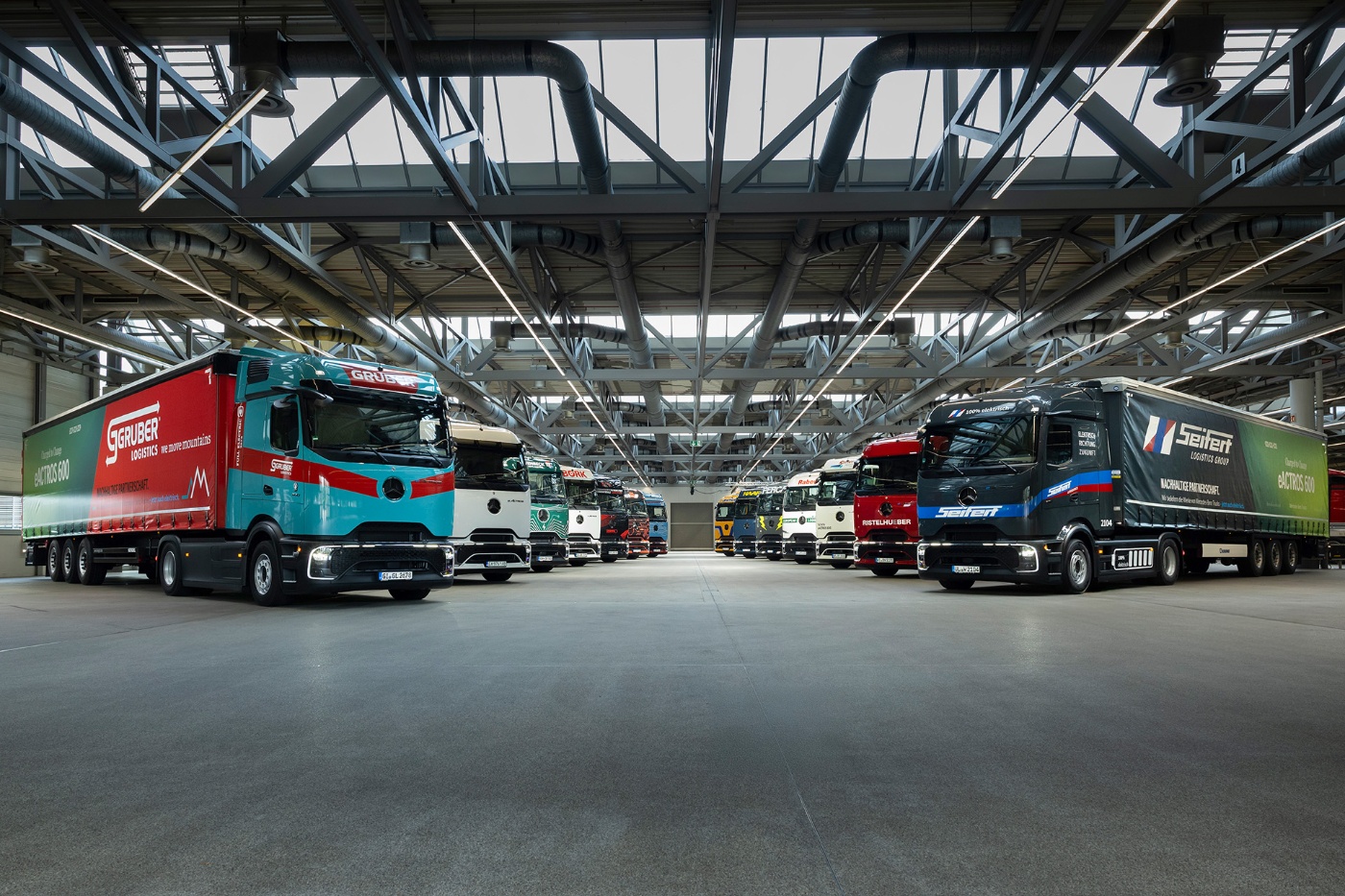 Mehrere große Lkw stehen nebeneinander in einer geräumigen, modernen Industriehalle.