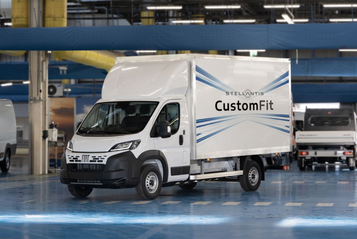 Ein weißer Fiat-Lieferwagen mit „CustomFit“-Aufdruck steht in einer großen Produktionshalle.