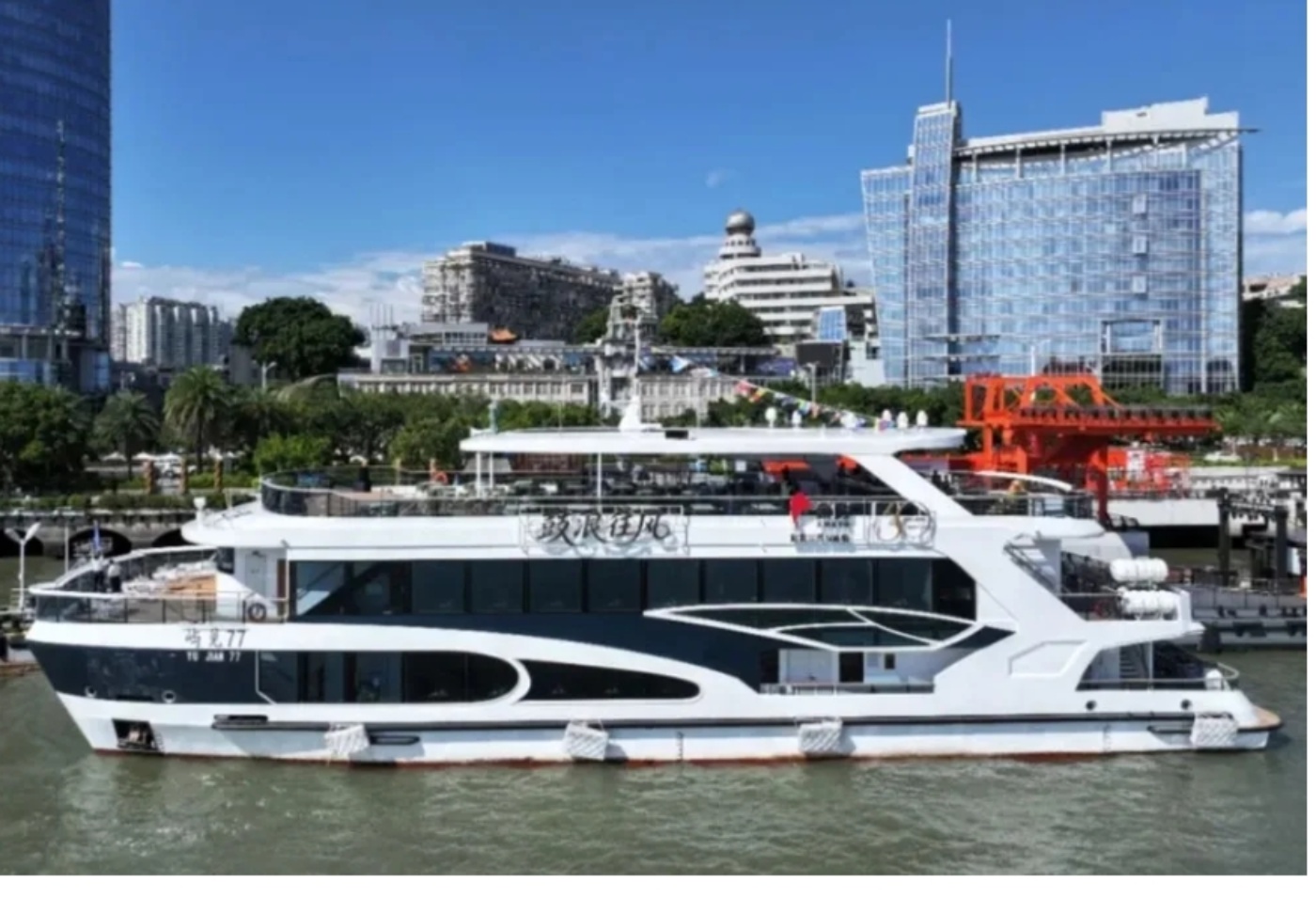 Modernes Flusskreuzfahrtschiff liegt an einem Stadtufer mit hohen Gebäuden im Hintergrund.