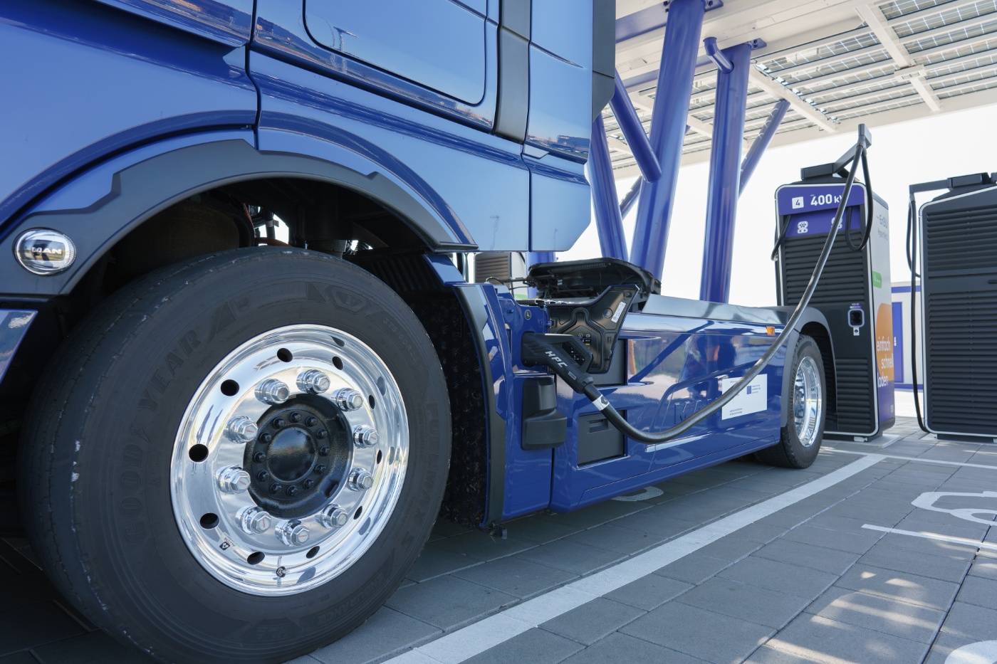 Blue electric truck charging at a public charging station.