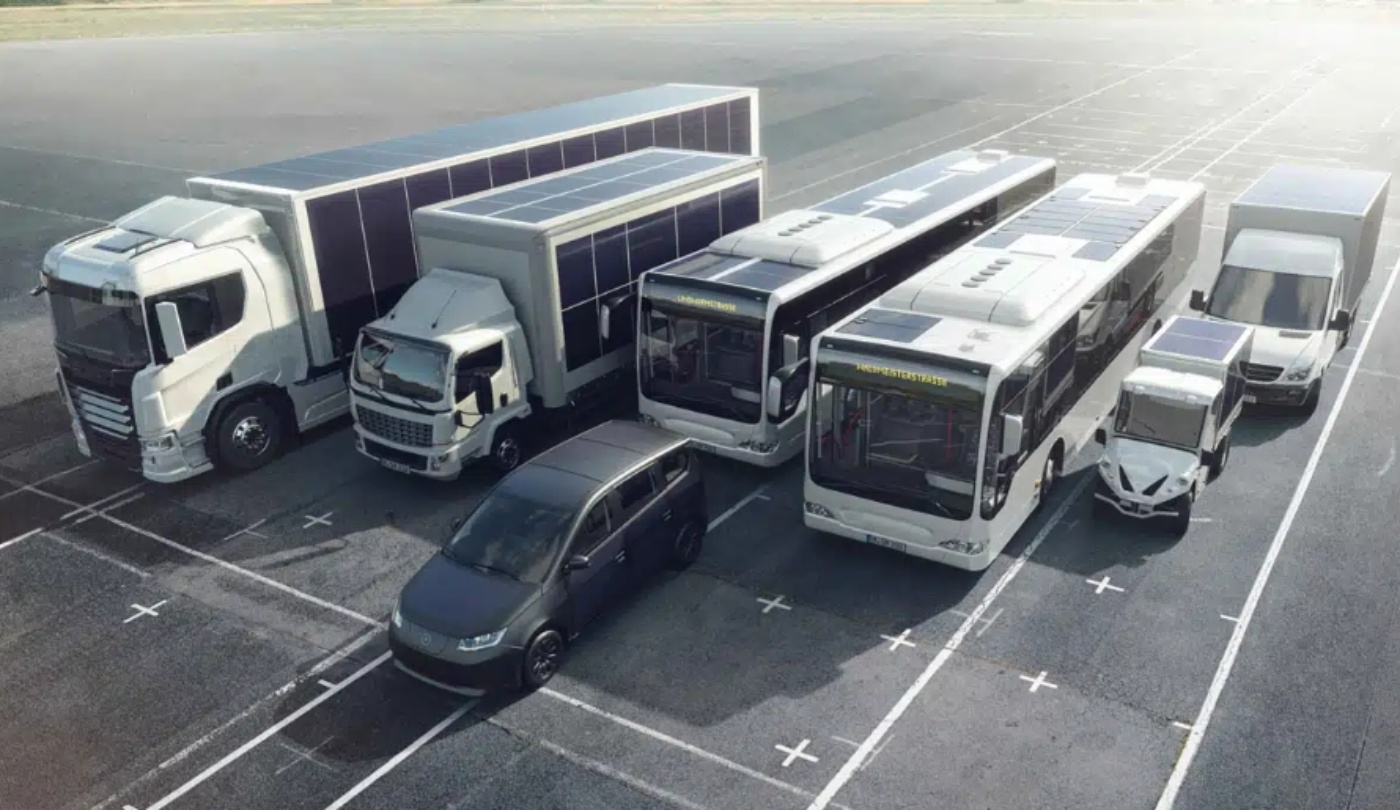 Several solar-powered electric vehicles, including buses and trucks, parked in a lot.