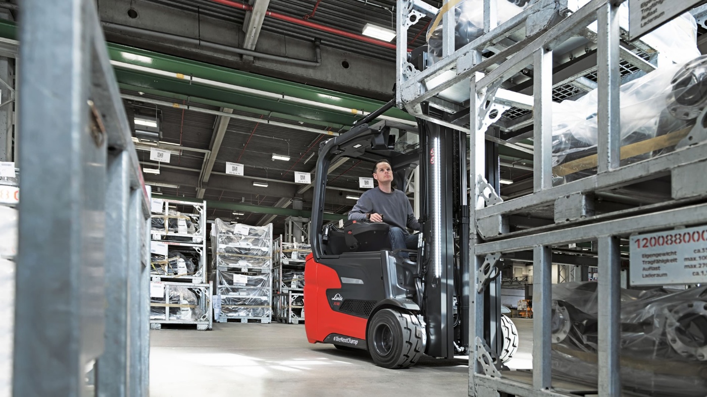 Worker operating a red forklift in a warehouse with stacked metal racks.