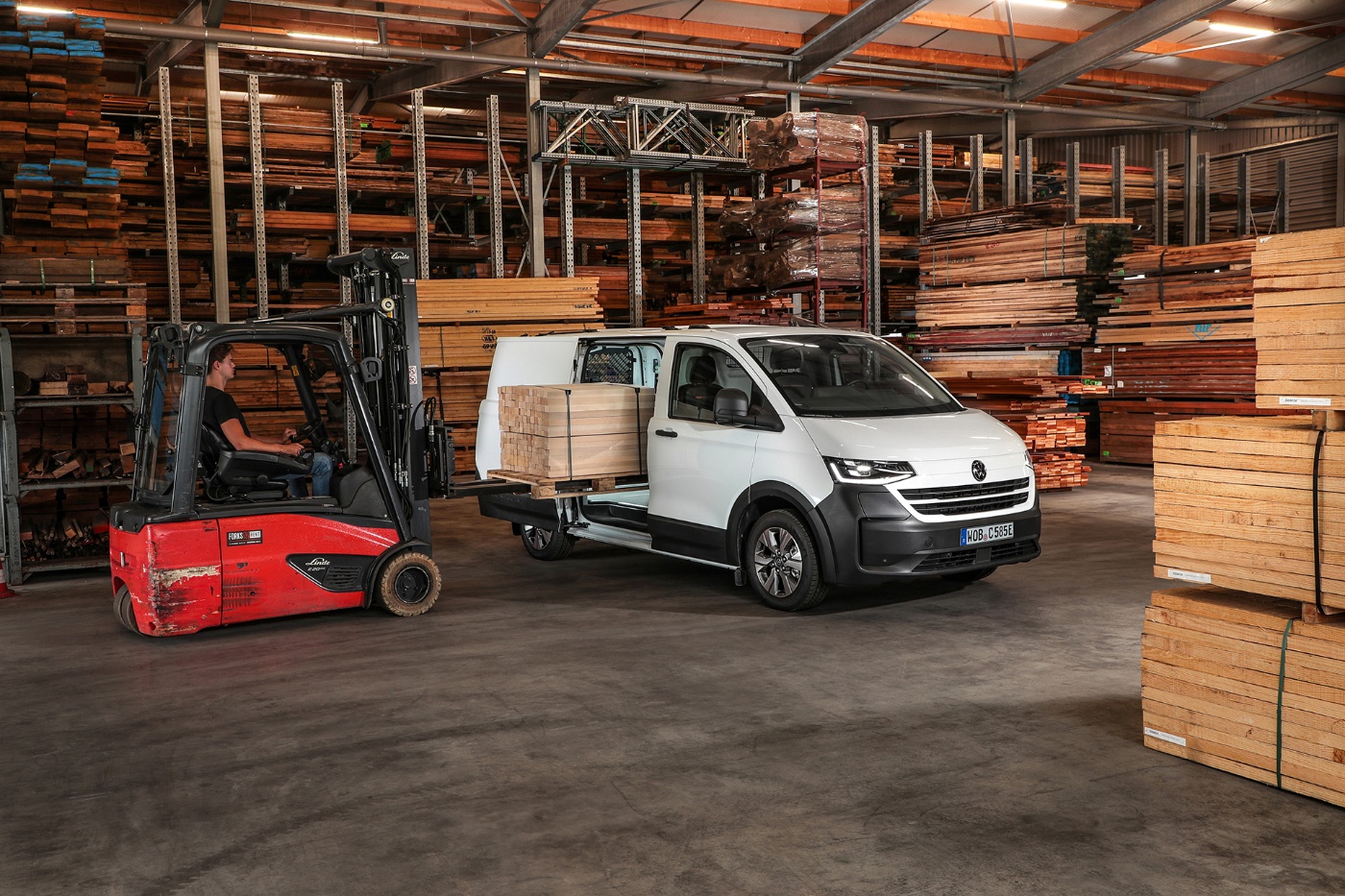 A forklift loads wooden boards into a white delivery van inside a timber warehouse.