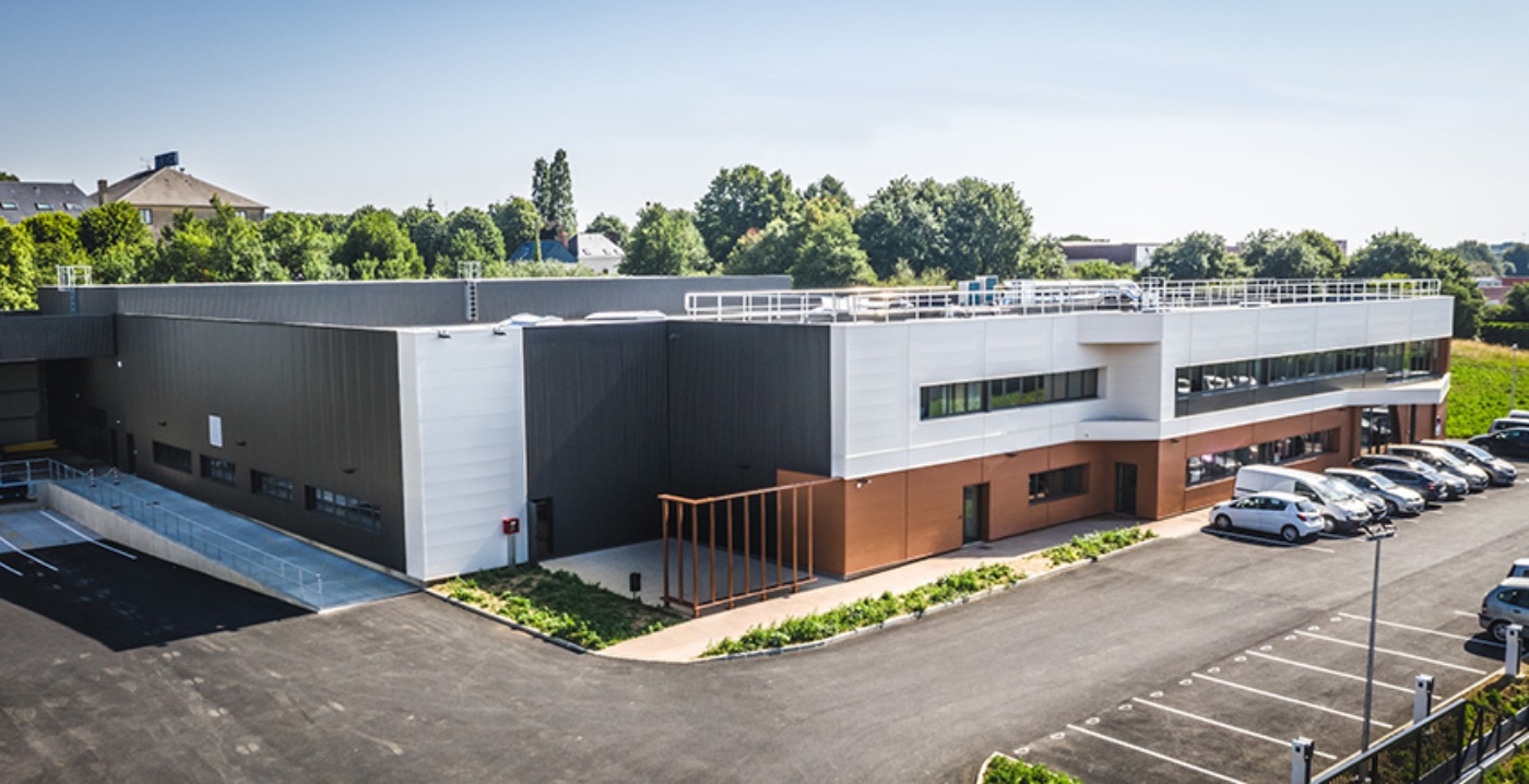 Modern industrial building with parking spaces and a ramp, surrounded by greenery.