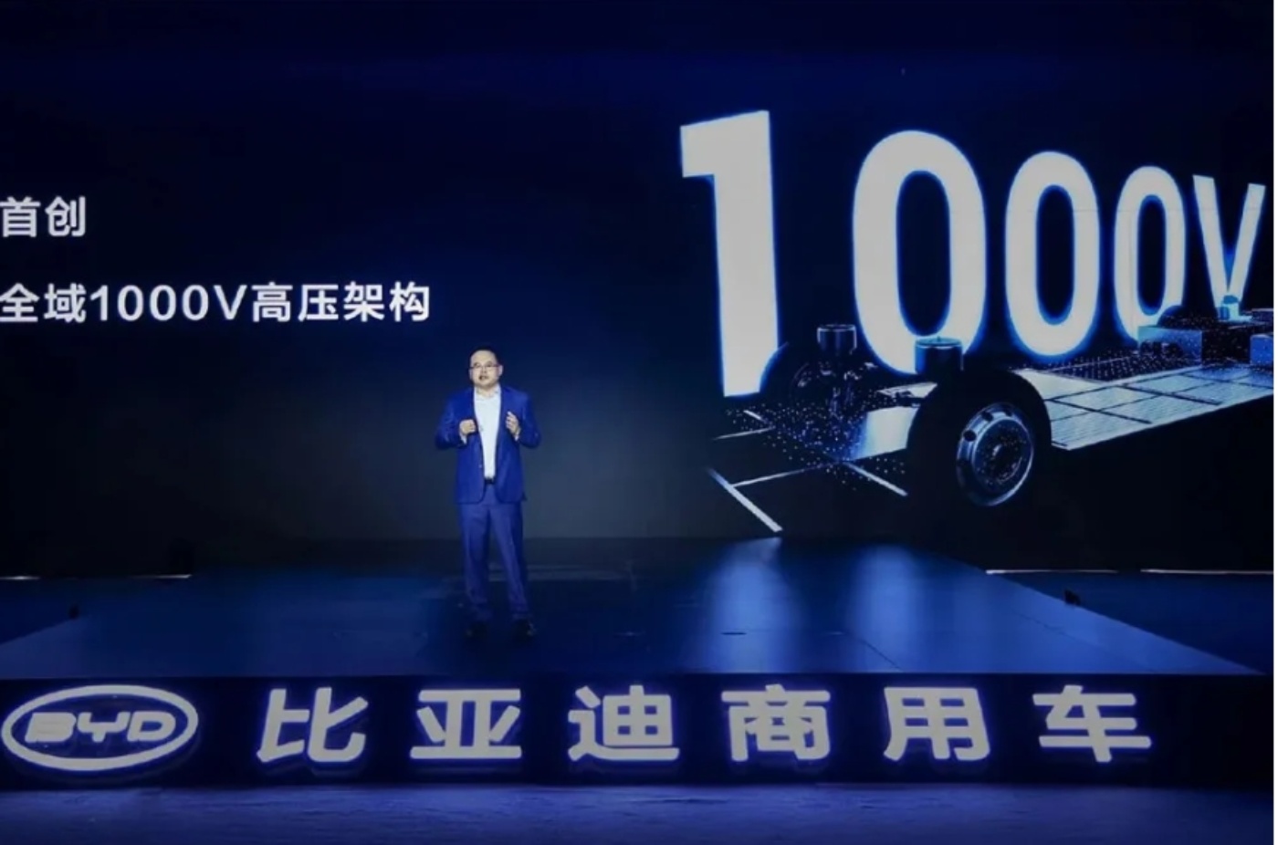 A man on stage presents BYD's new 1000V electric vehicle platform with a large screen display.