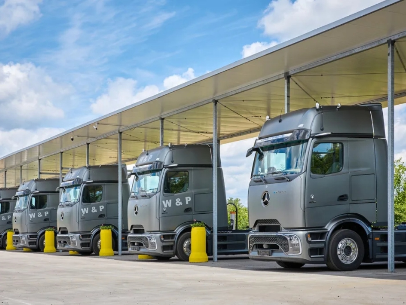 Several electric Mercedes-Benz trucks with W&P branding are parked under a covered charging area.