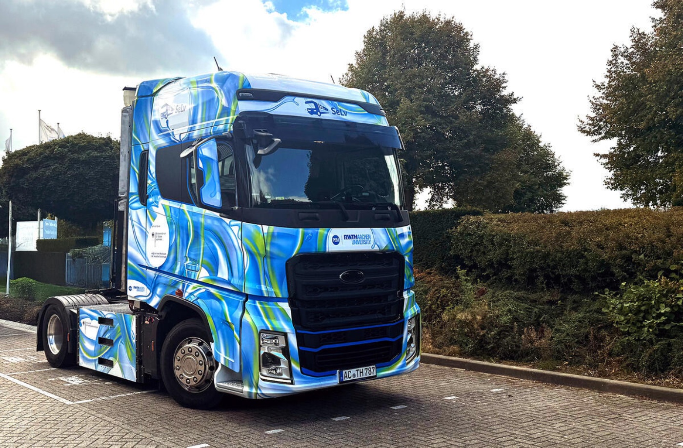 Colorfully wrapped truck with RWTH Aachen University logo parked on a street near trees.