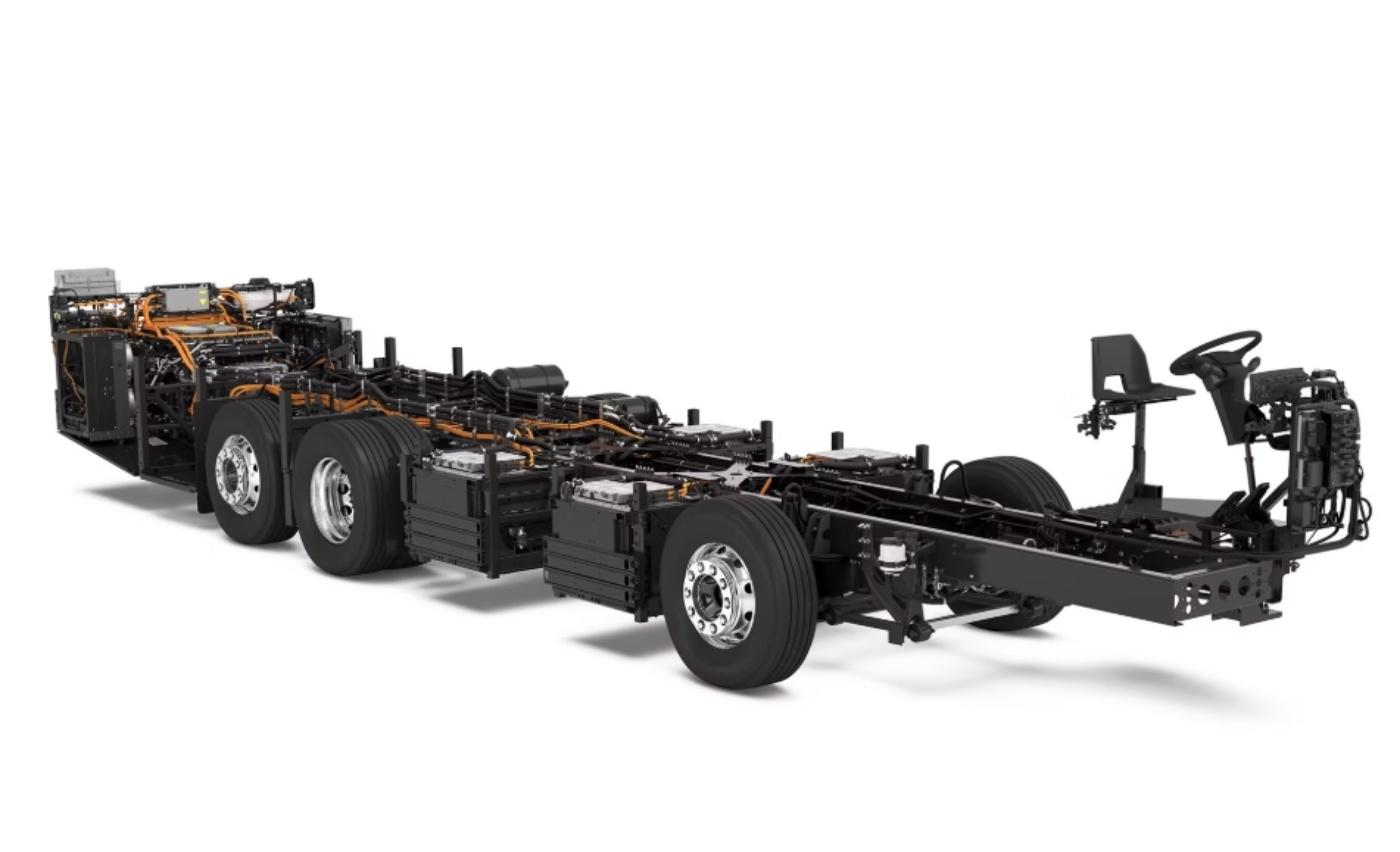 Electric bus chassis with exposed components, wiring, and driver's seat on a white background.