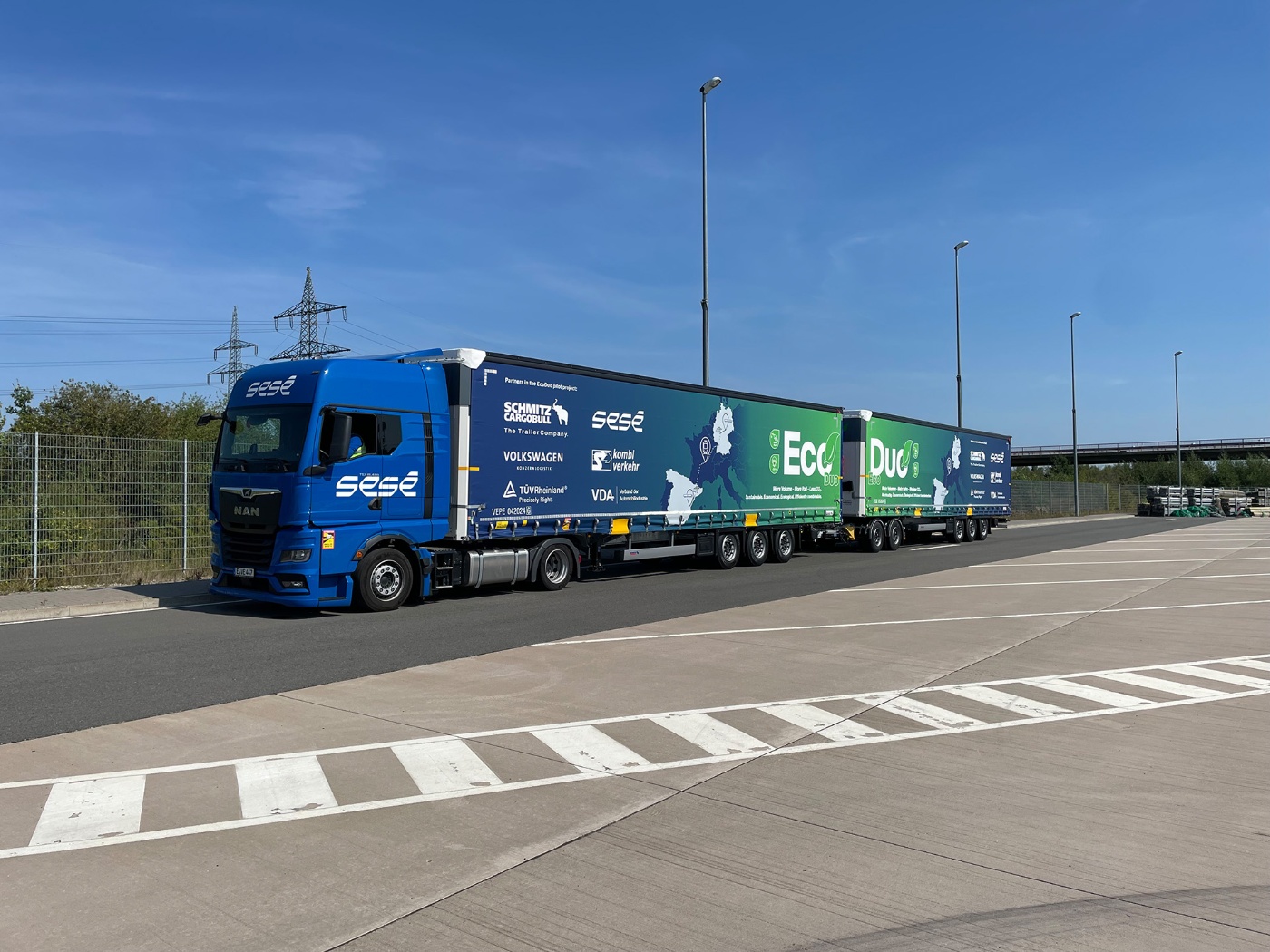 A long EcoDuo truck with company logos is parked on an industrial lot under a clear sky.
