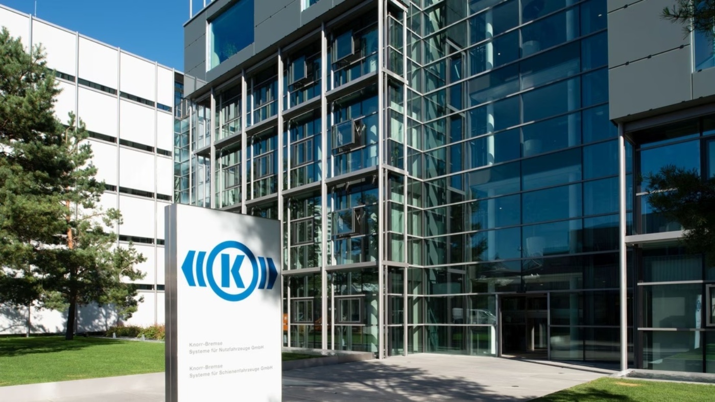 Glass facade of a modern office building with Knorr-Bremse logo on a white sign in the foreground.