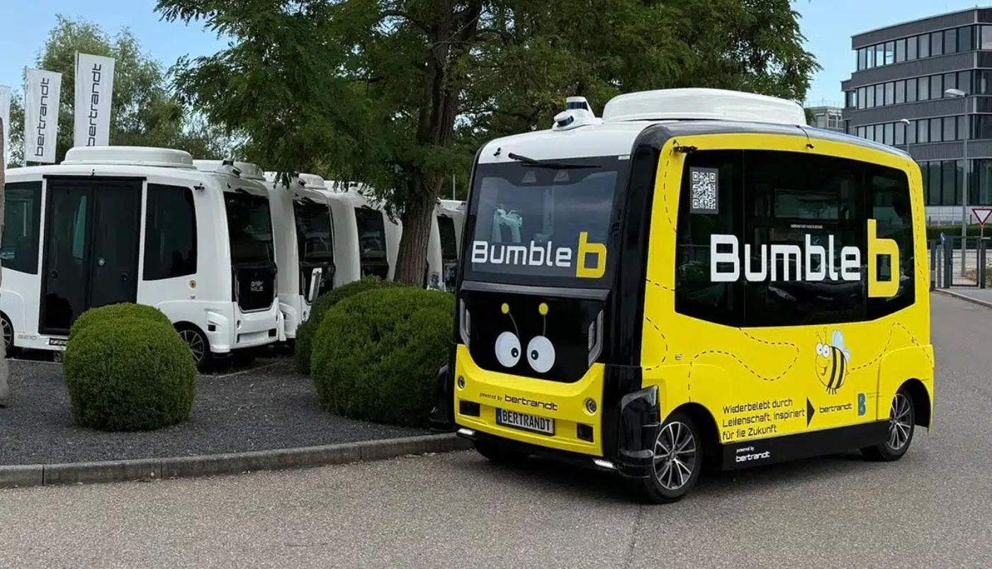 Gelber autonomer Shuttle „Bumble b“ steht neben mehreren weißen Shuttles.