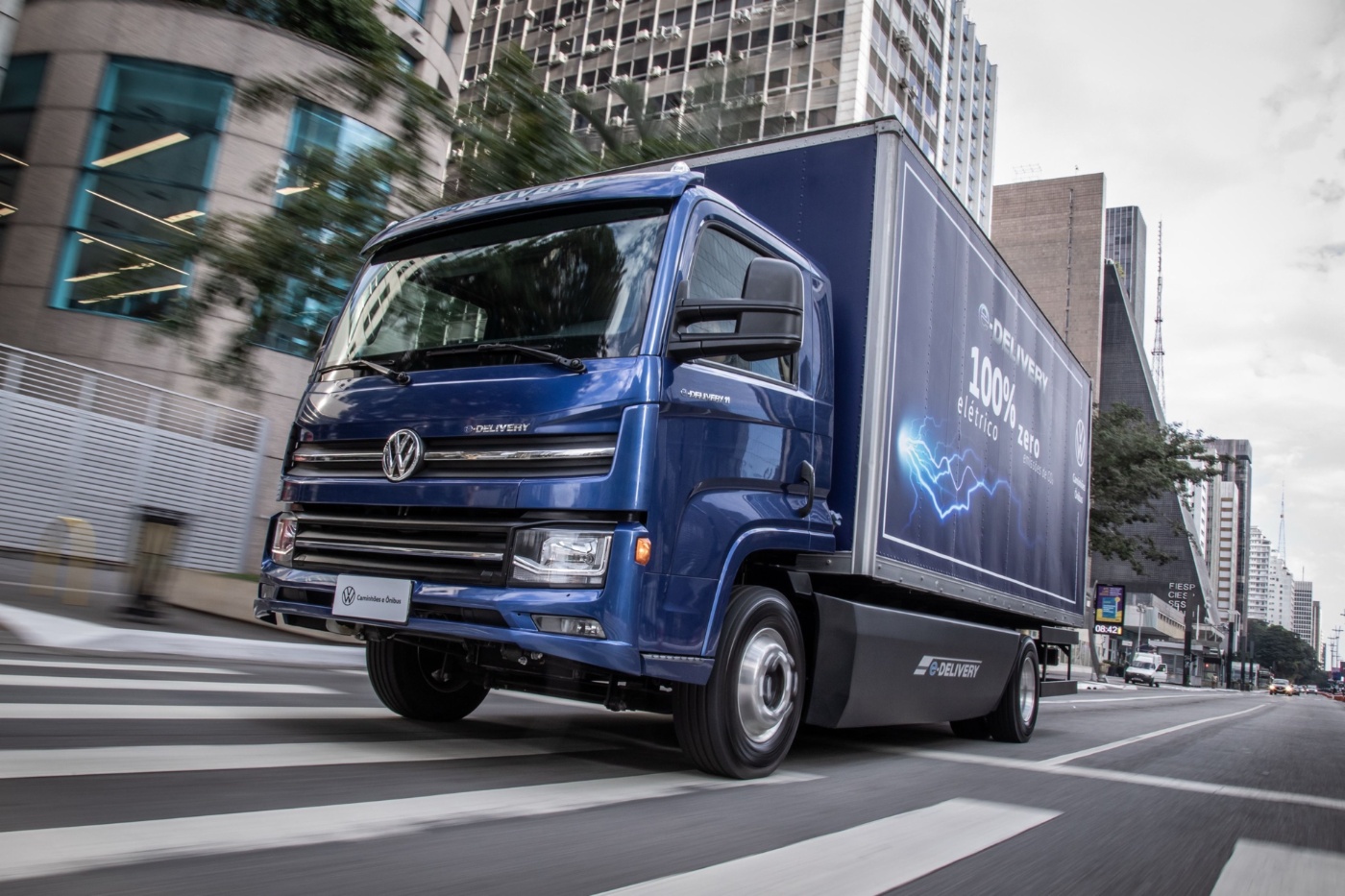 Electric Volkswagen delivery truck driving through a city with 100% electric branding.