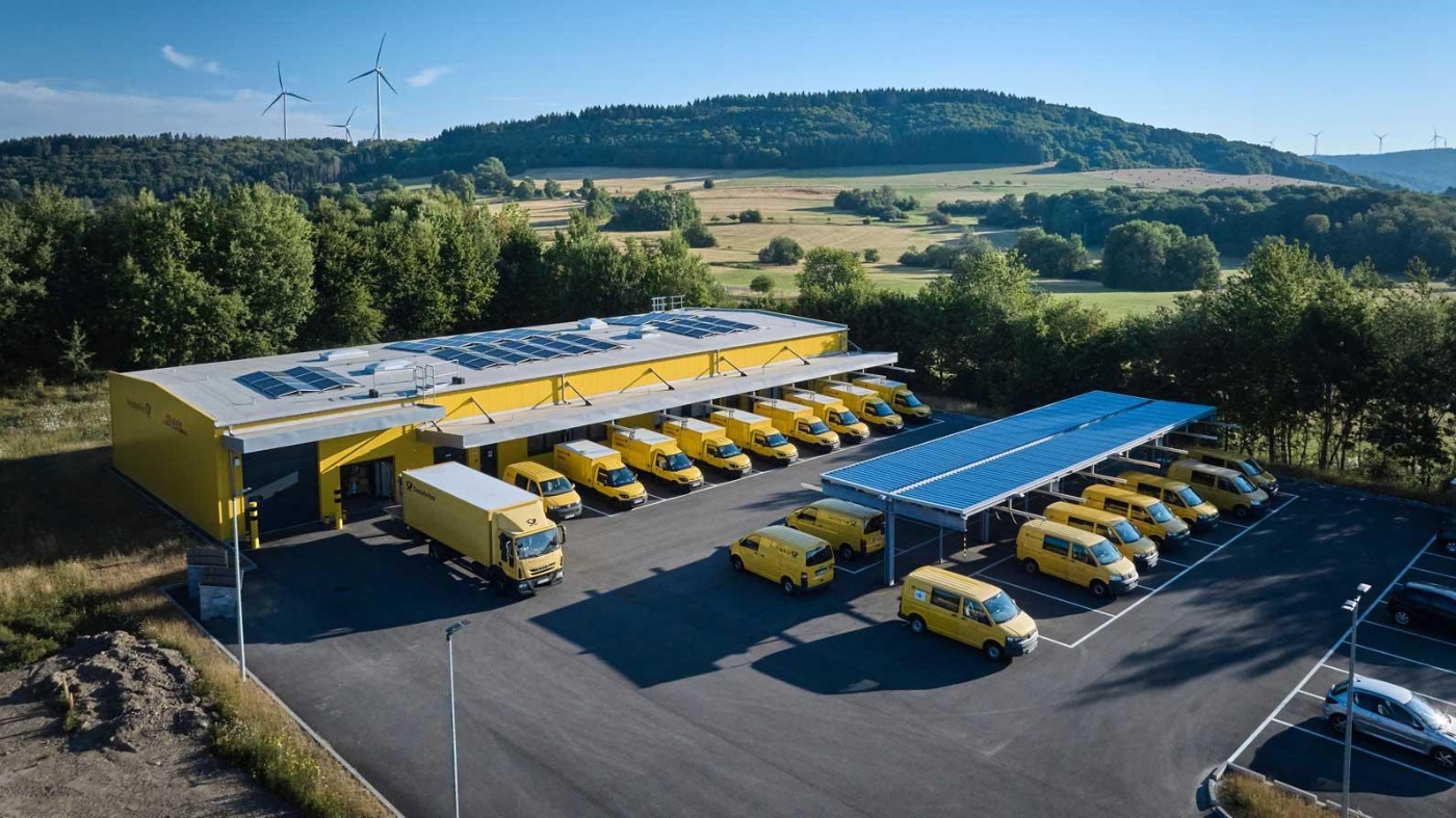 DHL logistics center with solar panels and multiple yellow delivery vans in a rural area.