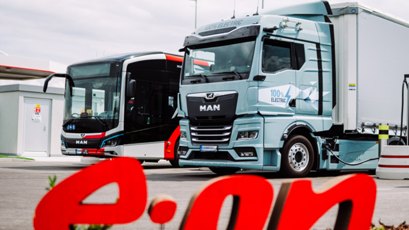 Electric MAN truck and bus are parked at a charging station, with E.ON logo in the foreground.