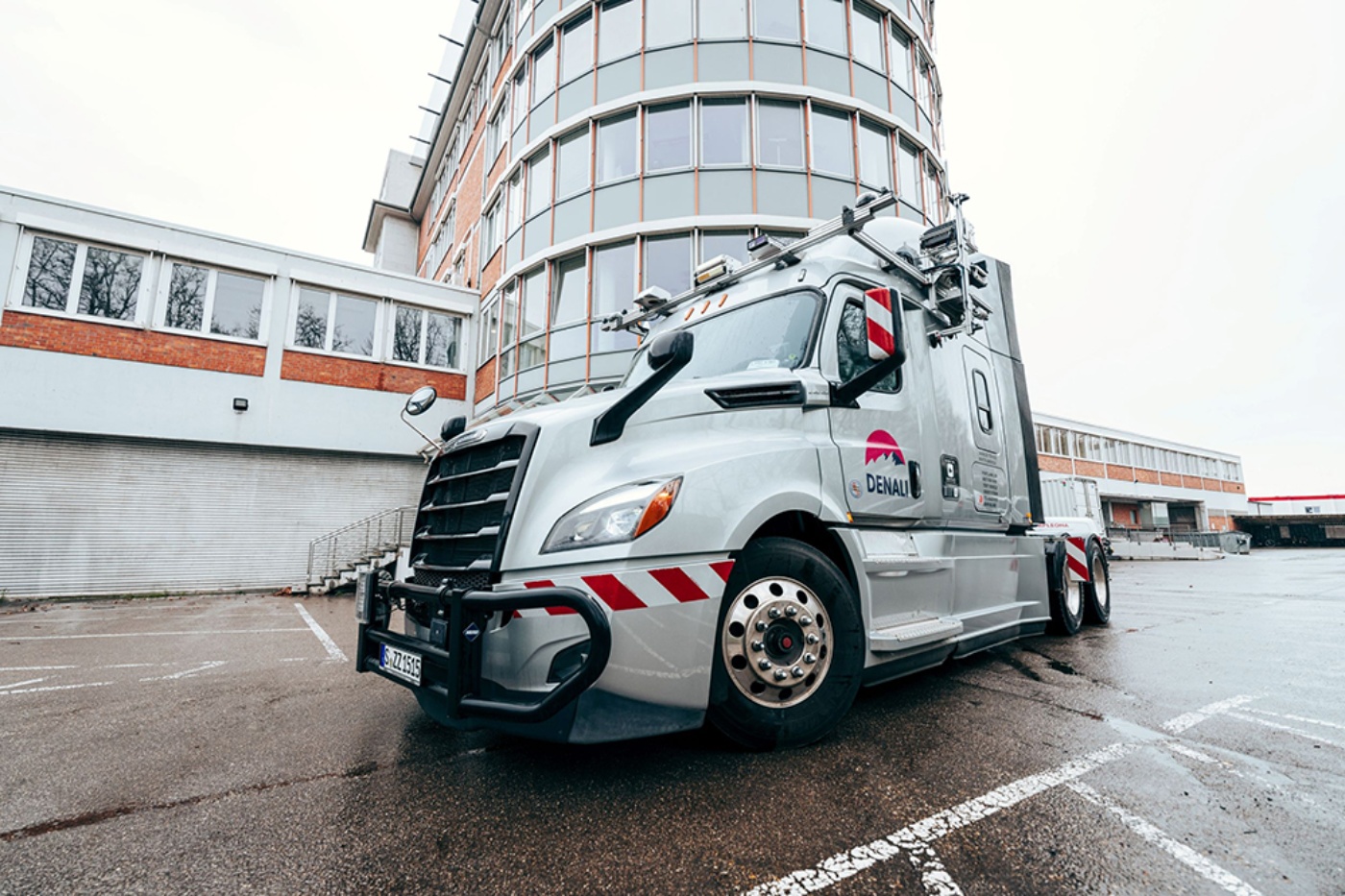 Silberner autonomer Test-Lkw mit Sensoren vor einem modernen Bürogebäude.