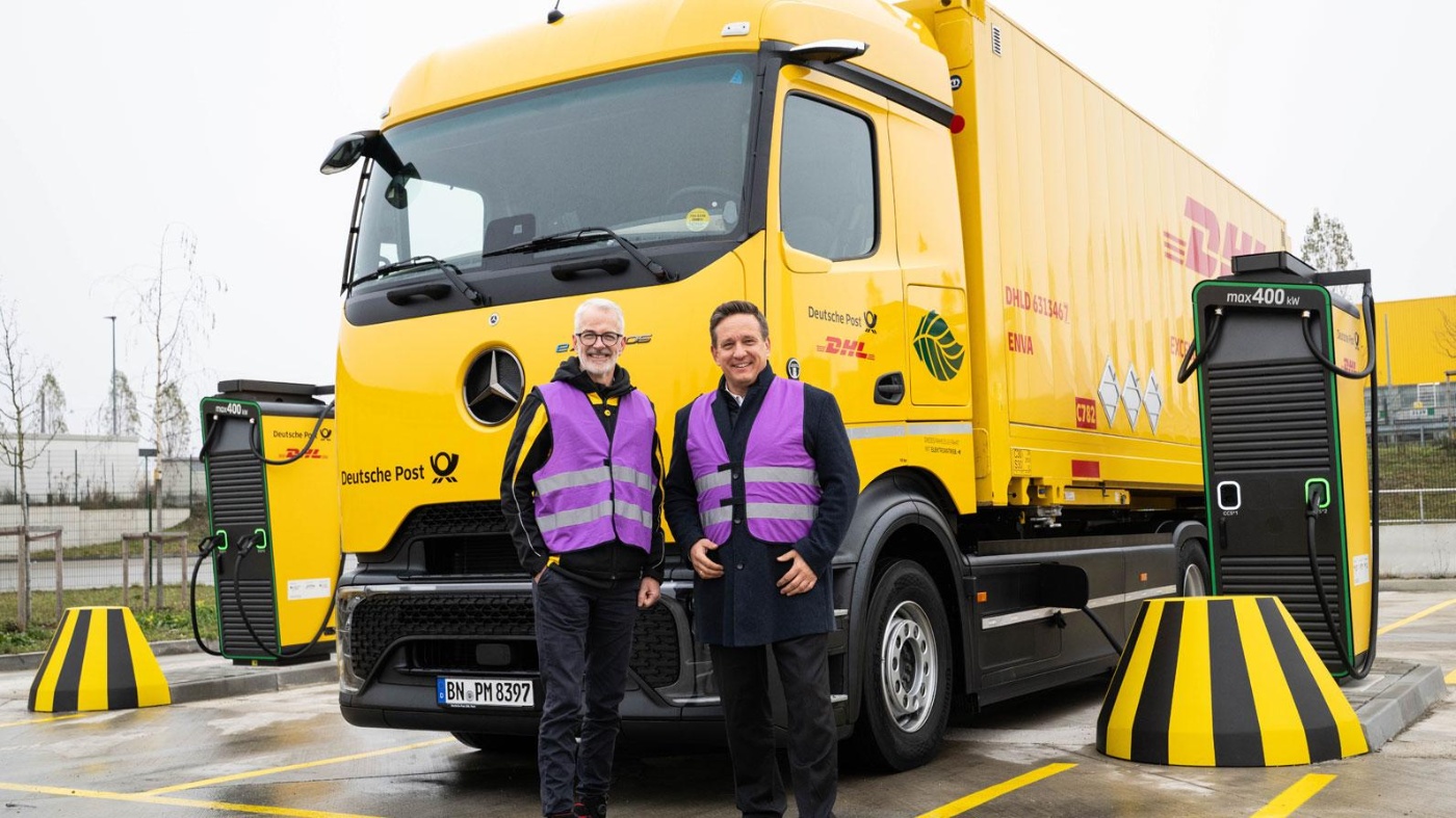Zwei Männer in Warnwesten vor einem DHL-E-Lkw an einer Schnellladestation.