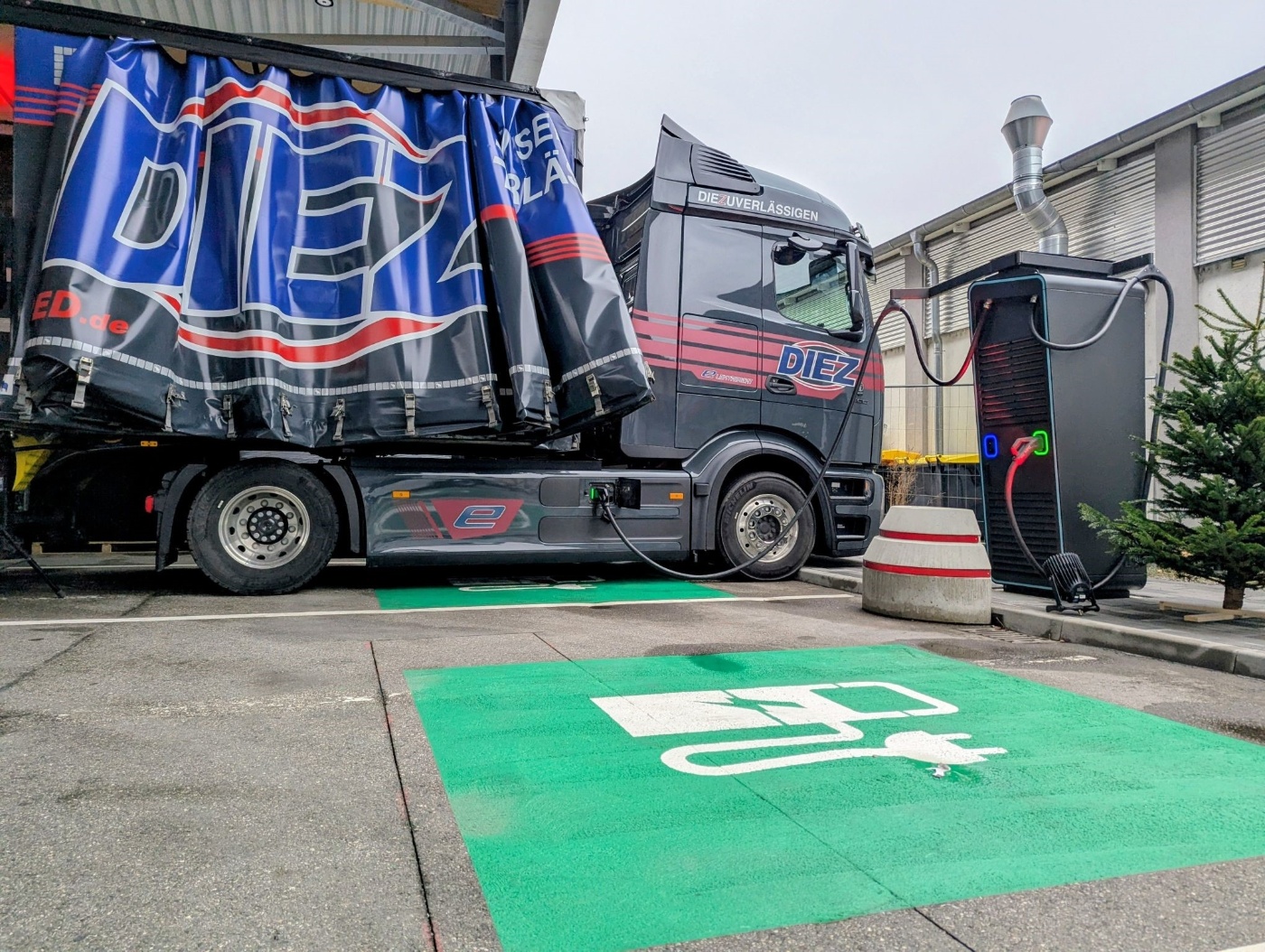 Ein Elektro-Lkw mit der Aufschrift „DIEZ“ lädt an einer grün markierten Ladestation.