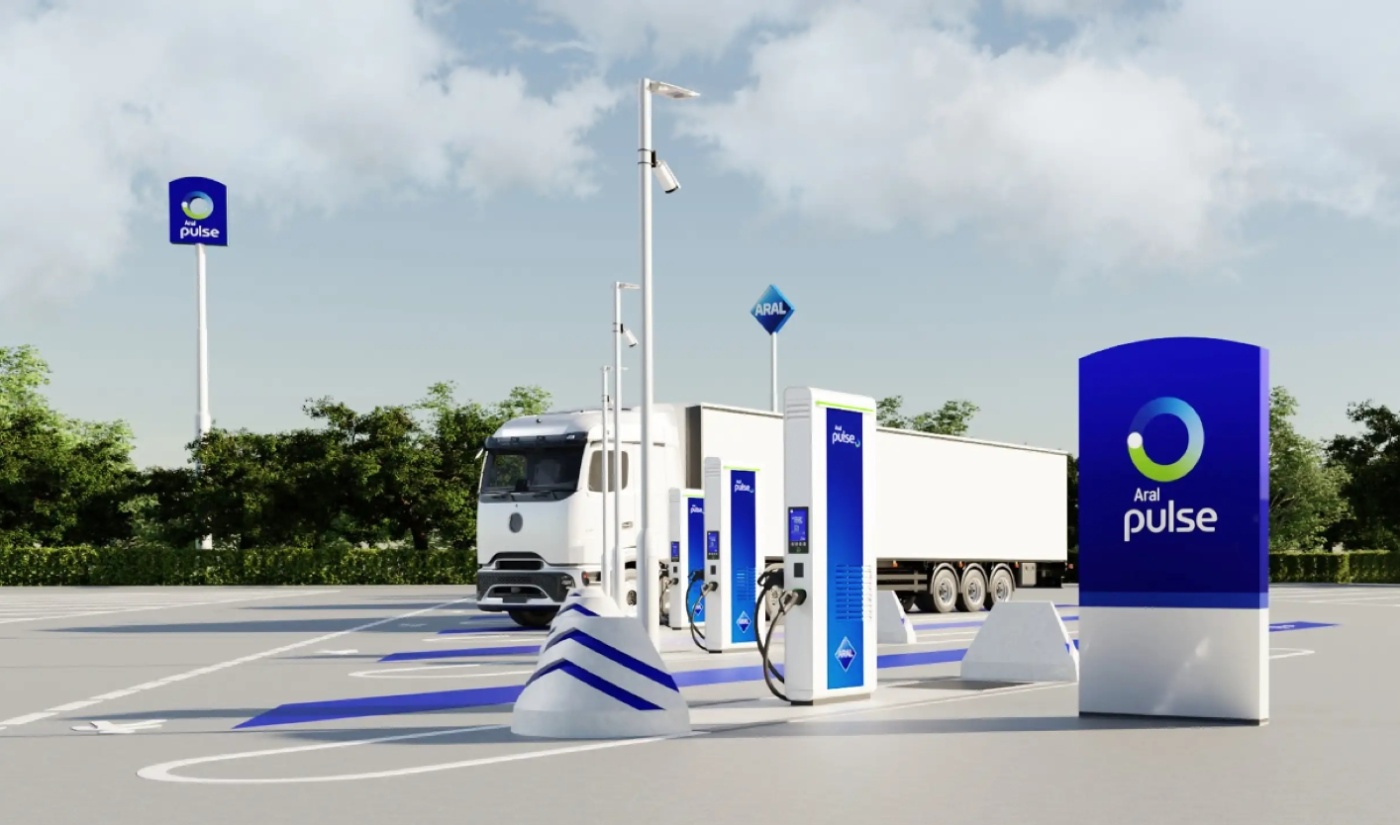 Ein weißer Elektro-Lkw steht an Aral-pulse-Ladestationen in einem modernen Rasthof.