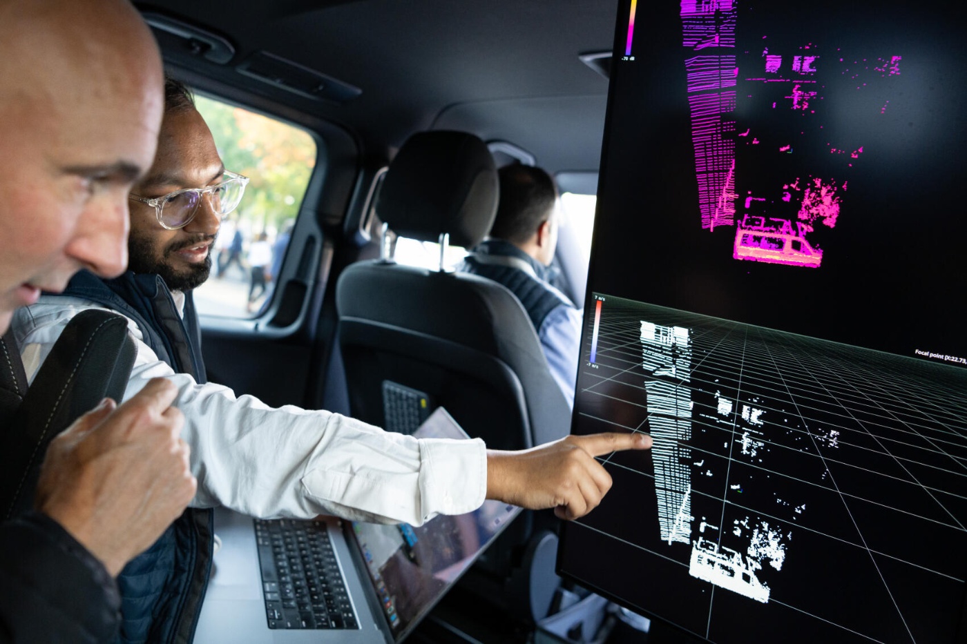Zwei Männer im Auto analysieren 3D-Sensordaten auf einem Bildschirm, vermutlich zu Autonomietechnik.