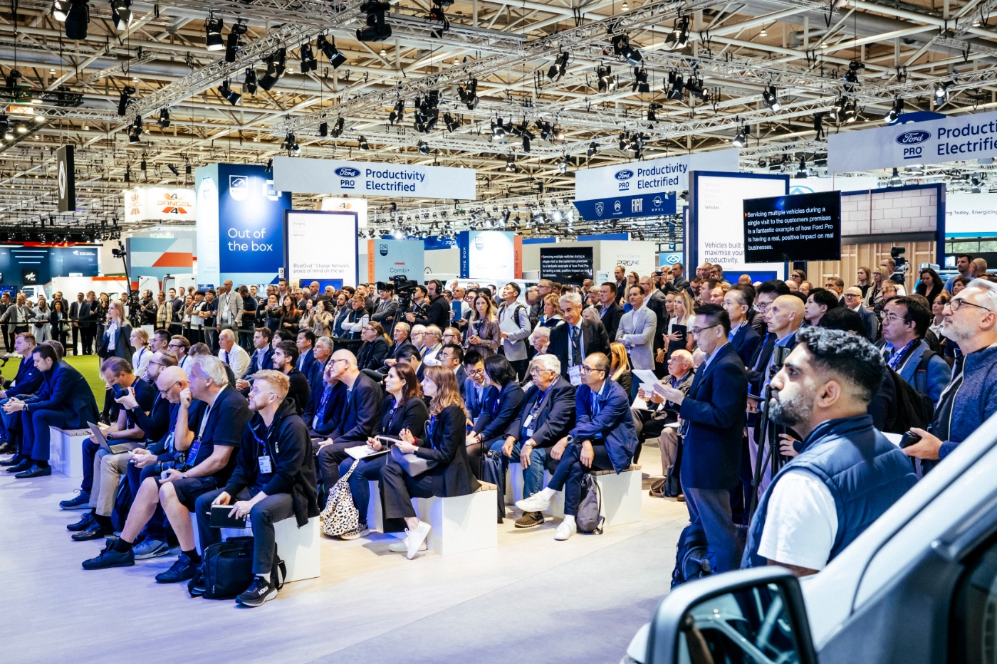 Audience at a Ford Pro trade show booth listening to a presentation on electrified productivity.