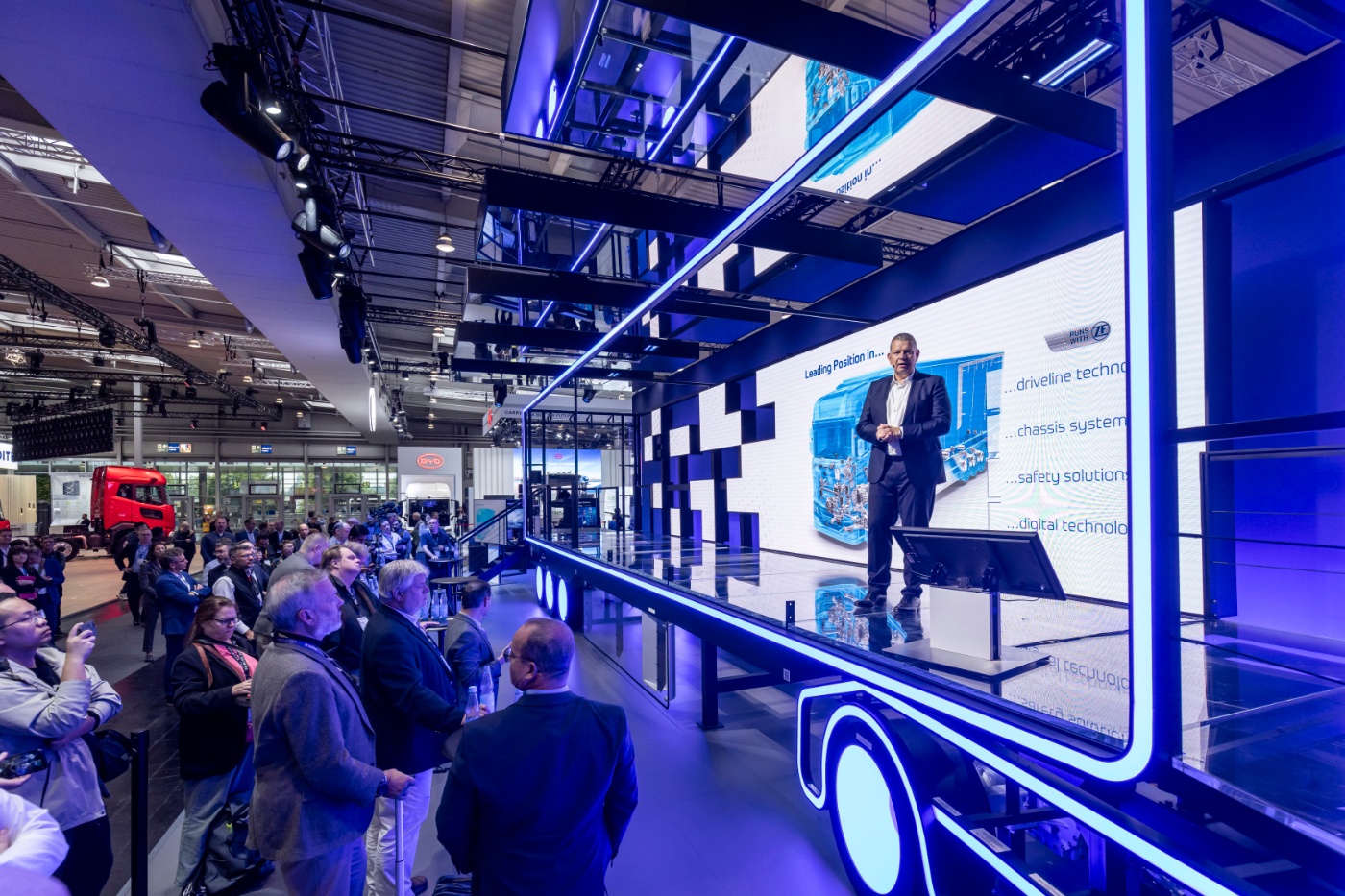 Speaker presenting drivetrain technology on a stage at a trade show.