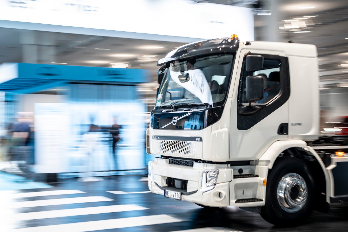 White Volvo electric truck driving indoors at a trade fair.