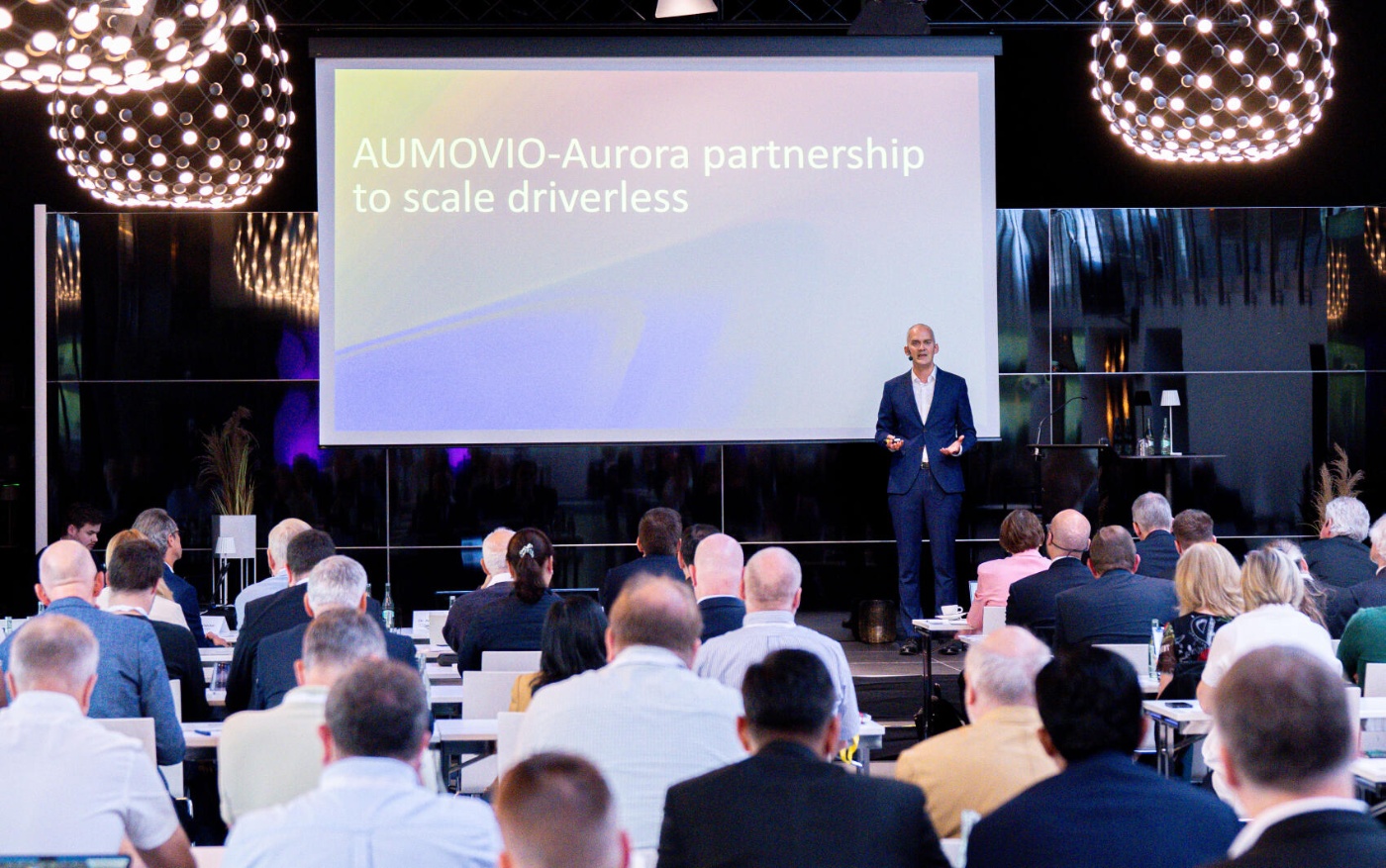 A man presents the AUMOVIO-Aurora partnership to scale driverless trucks.