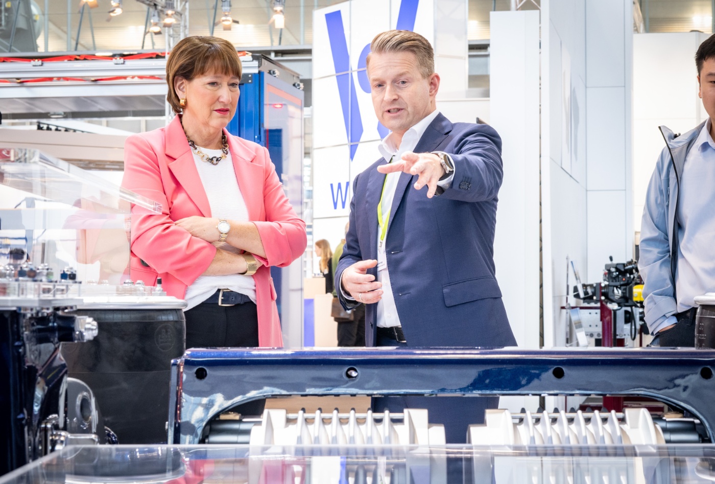 A man presents industrial equipment Hildegard Müller at a trade fair booth.