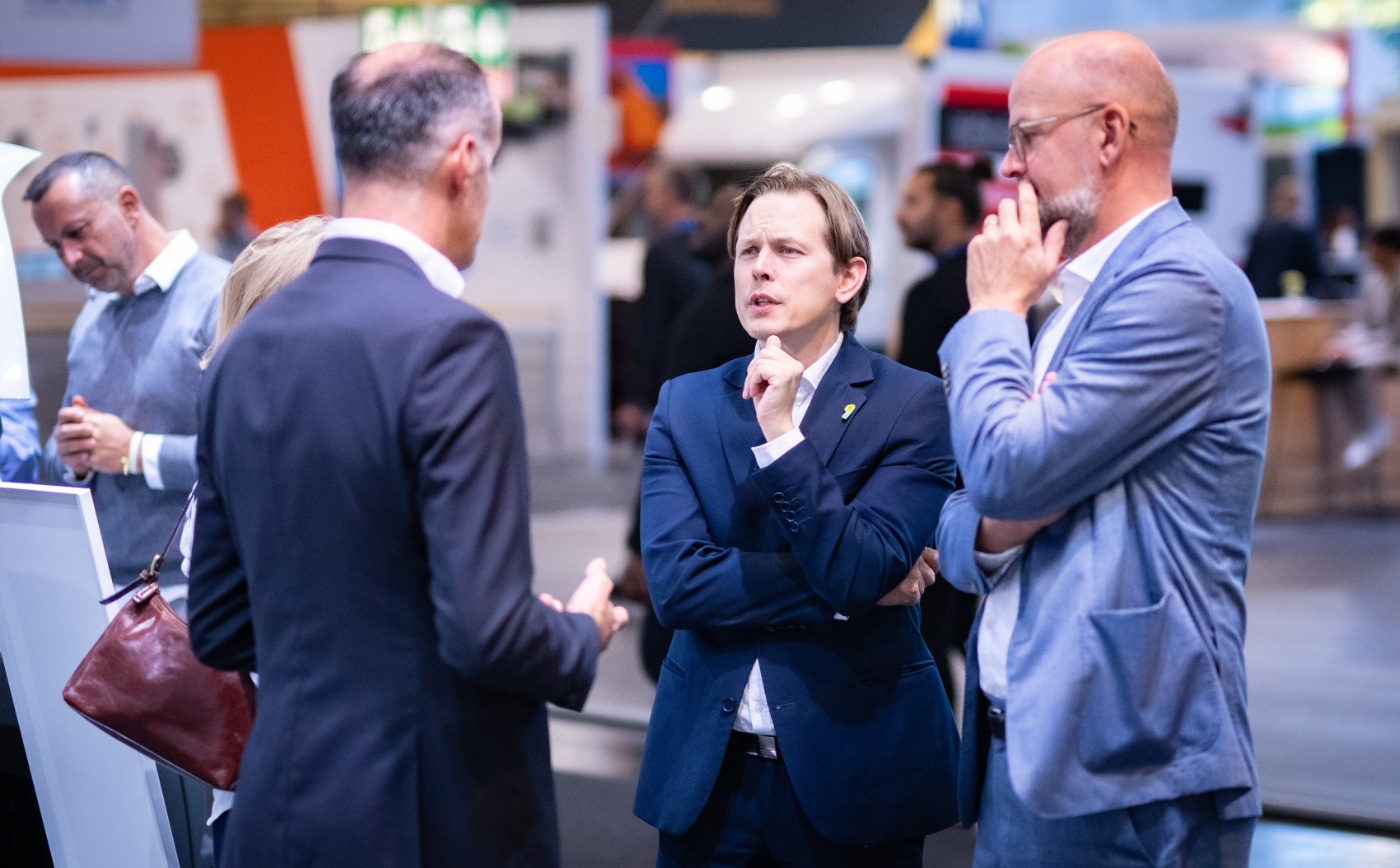 Business professionals discuss at a trade fair or conference booth.