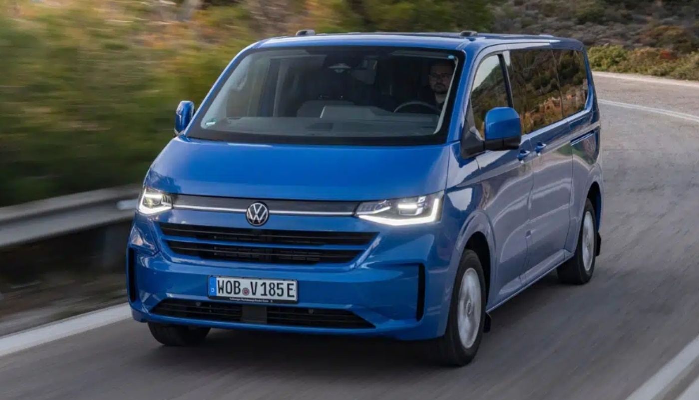 Ein blauer Volkswagen-Transporter fährt auf einer Kurve, der Fahrer ist sichtbar.