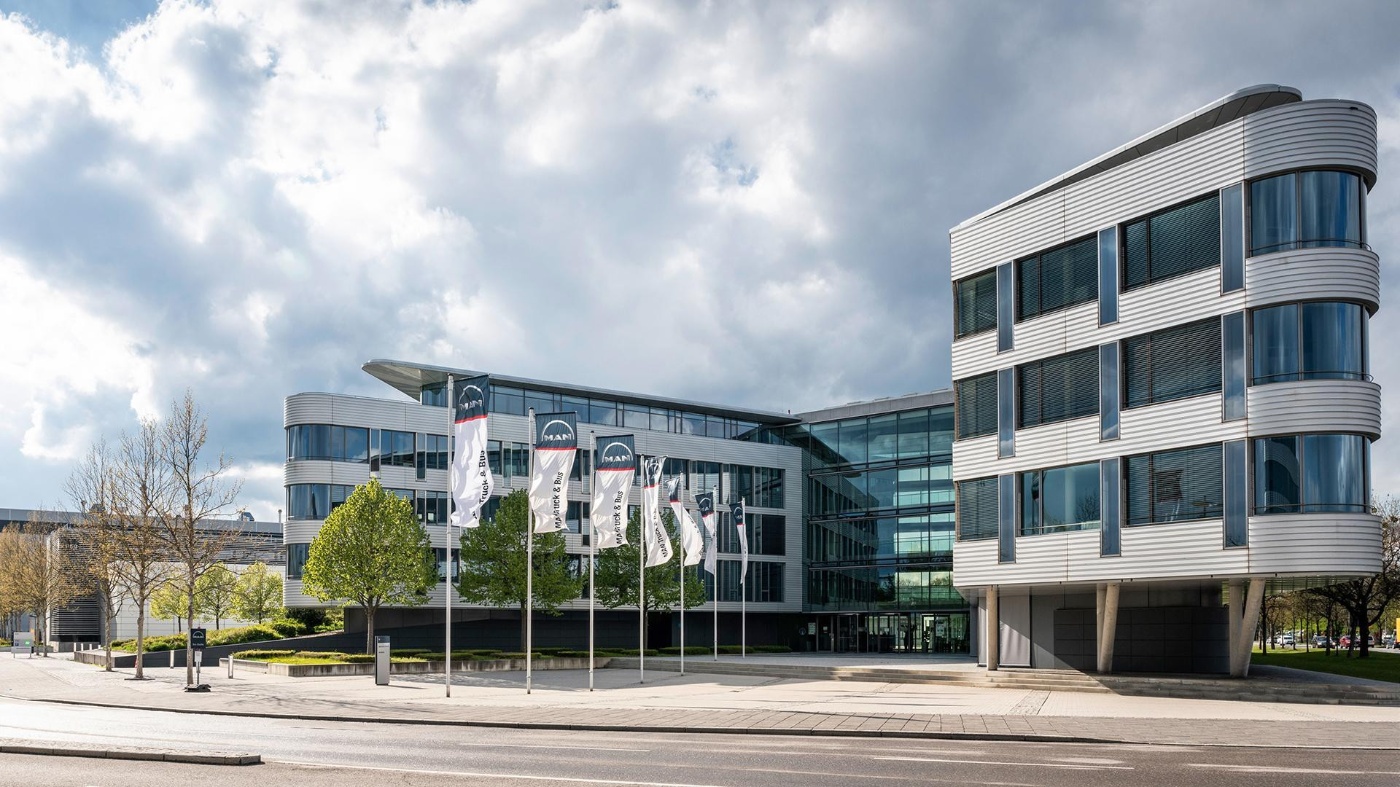 Modern office building with glass facade and MAN Truck & Bus flags in front.