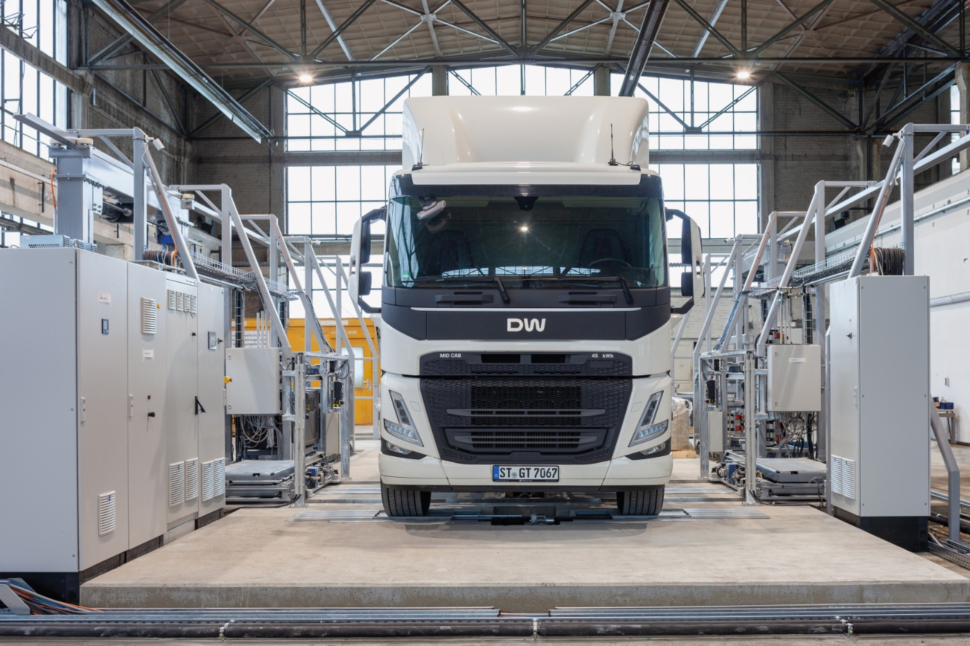 Electric truck in a test hall, surrounded by technical equipment and control cabinets.