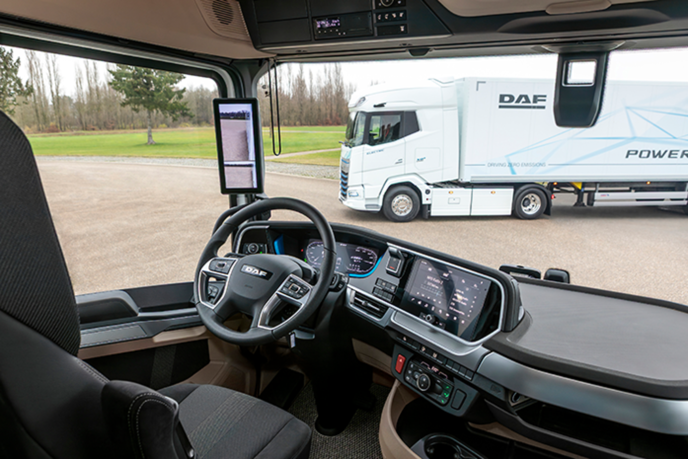 View from inside a DAF truck cab with digital dashboard, looking out at another DAF truck.