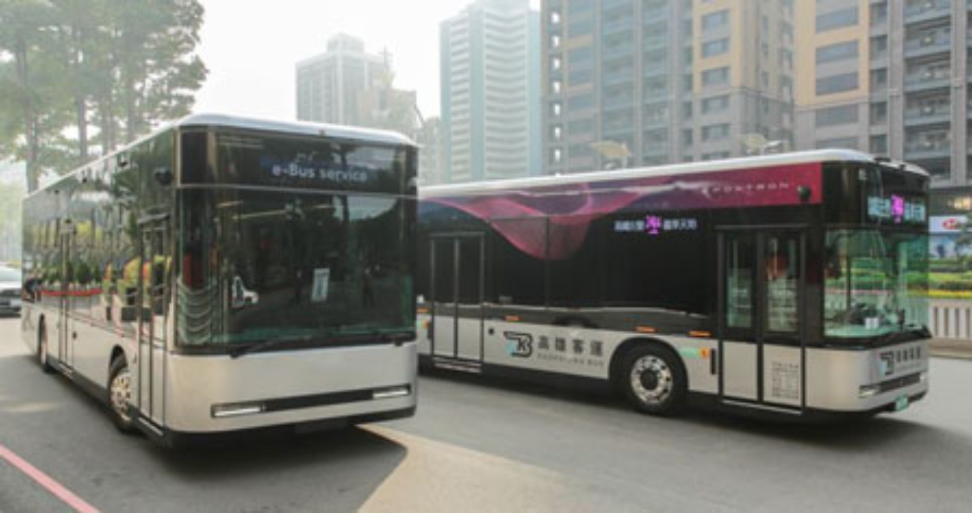 Zwei moderne Elektro-Stadtbusse von Foxconn auf Straße mit Hochhäusern im Hintergrund.