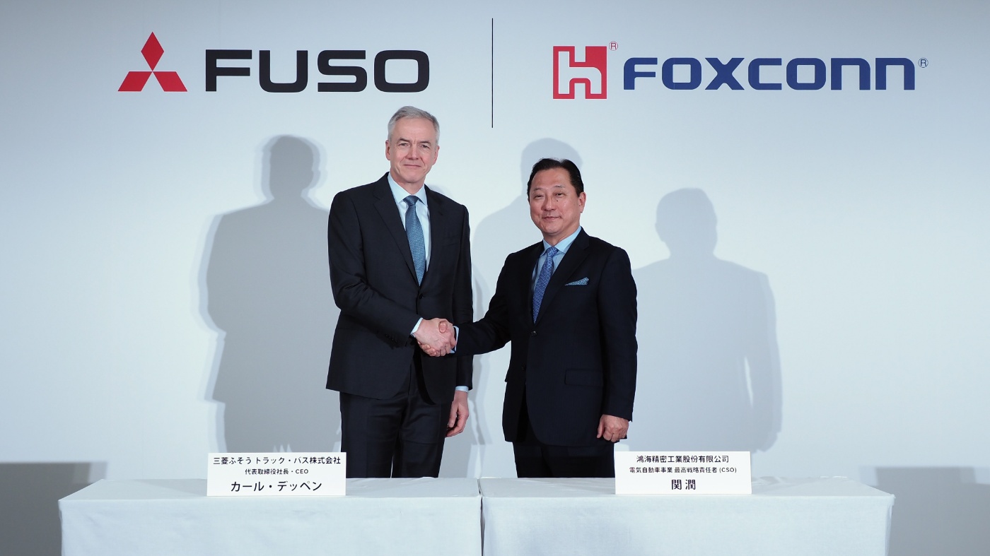 Executives from FUSO and Foxconn shake hands in front of logos during a press event.